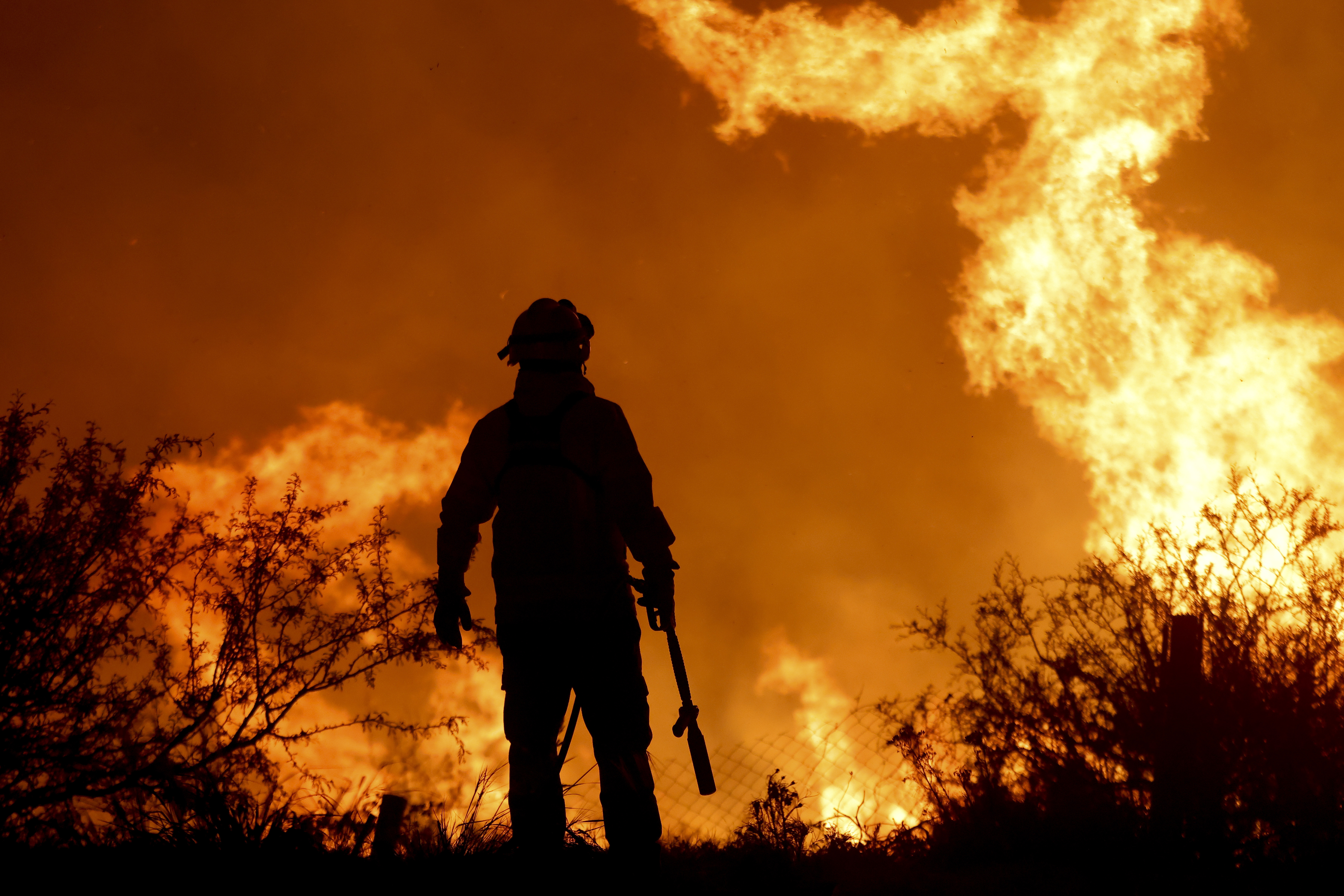 A firefighter is silhouetted by the flames of a forest fire on the outskirts of Villa Carlos Paz, Argentina