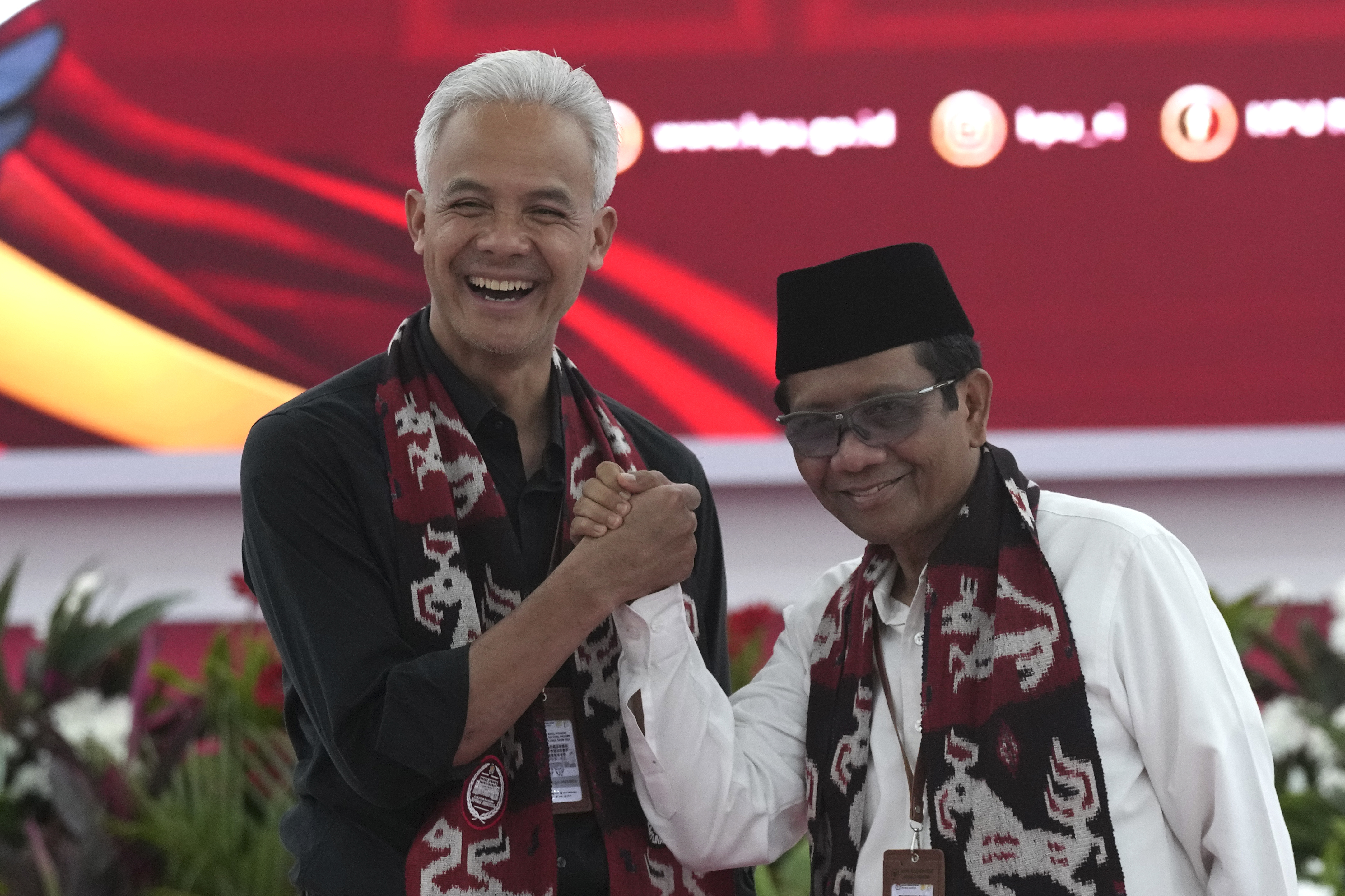 Presidential candidate Ganjar Pranowo (left) shakes hands with his running mate Mahfud MD. They are both smiling.