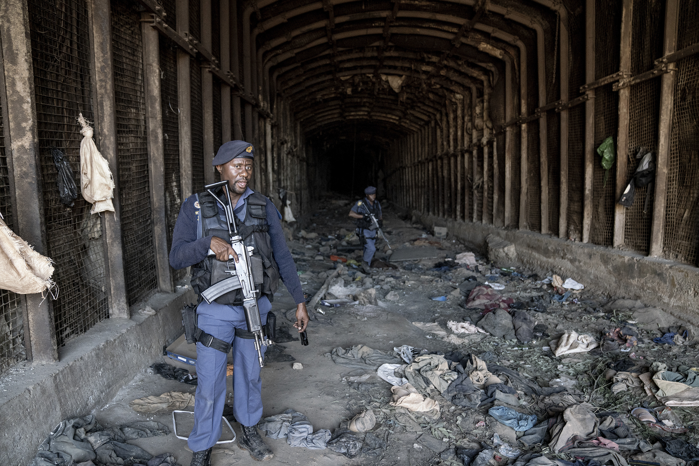 Members of the South African Police Service (SAPS) carry their weapons as they guard the entrance to an abandoned mine during an operation in Stormhill west of Johannesburg on August 10, 2023 where territorial battles between illegal miners known as Zama Zamas has wreaked havoc in the area claiming the lives of several miners. Five people have been shot dead in South Africa's Johannesburg in suspected violence between rival illegal mining gangs, police said Sunday. The five bodies, believed to be of illegal miners, were found near an abandoned mine shaft clsoe to a slum in the suburb of Riverlea west of Johannesburg. (Photo by Shiraaz Mohamed / AFP)