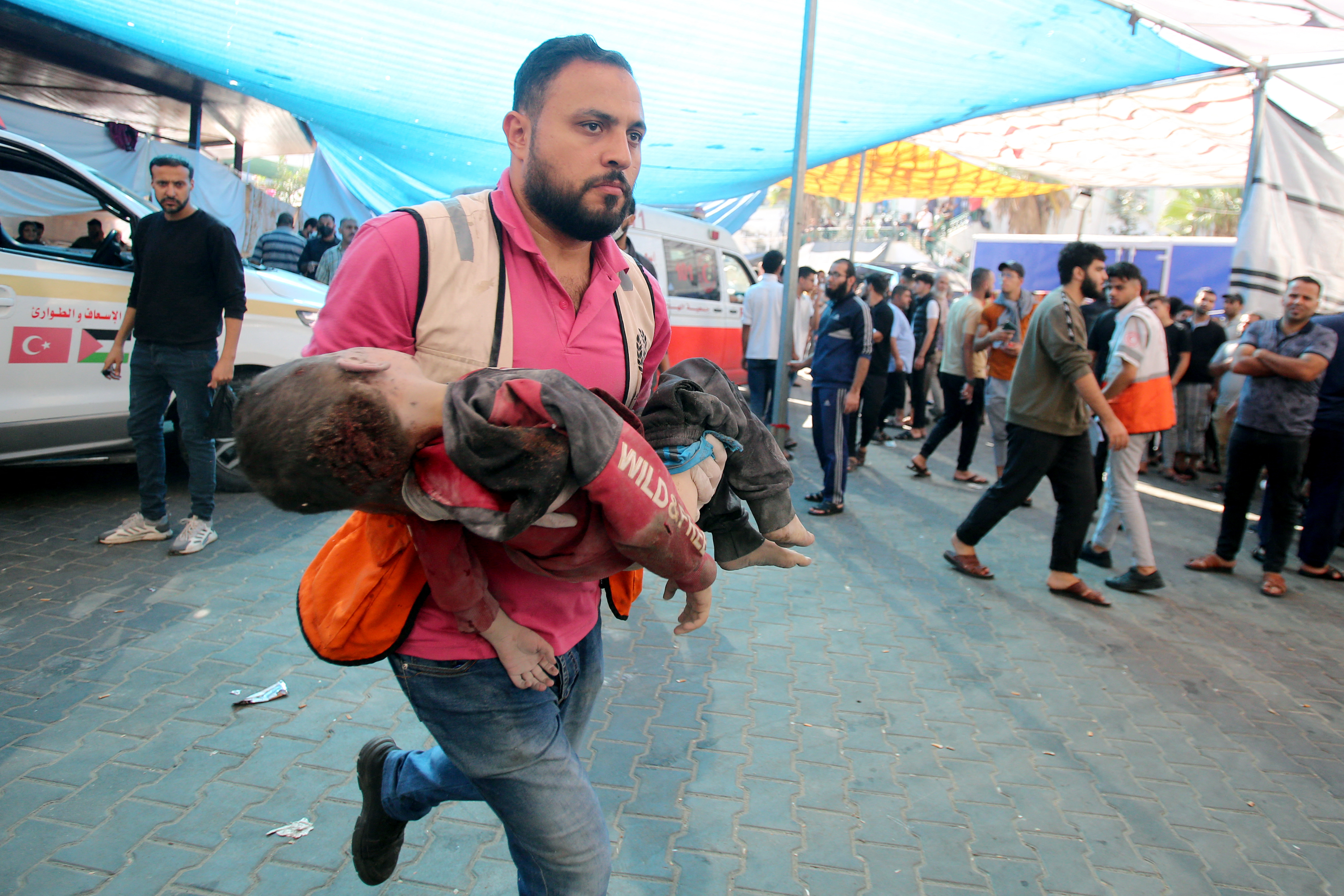 A man rushes with a toddler in his arms into Al-Shifa hospital following the Israeli bombardment of Gaza City's Mansura neighbourhood, in the eastern suburb of Shujaiya on November 4