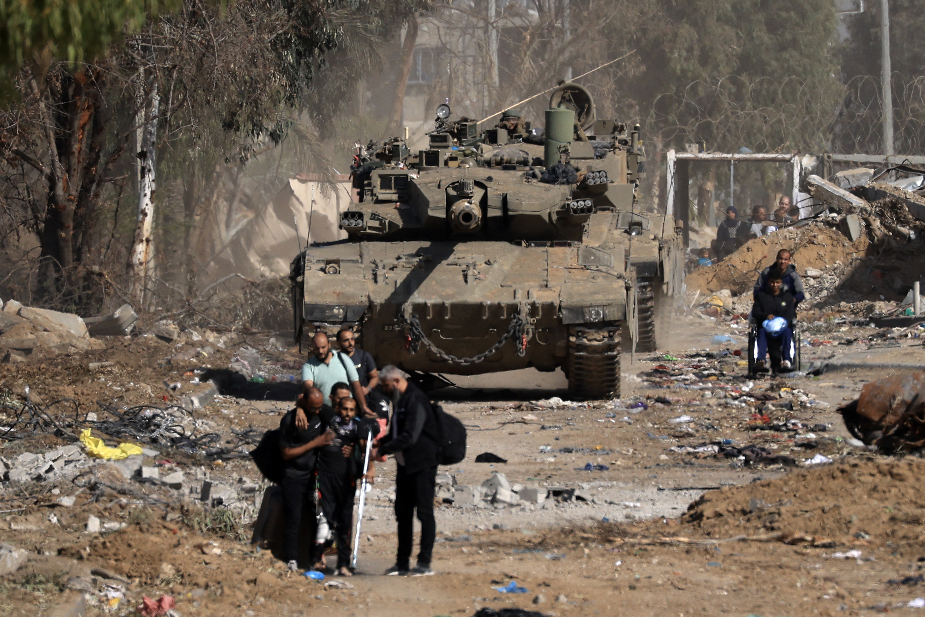 Palestinians, including poeple injured during the bombardment, pass an Israeli tank