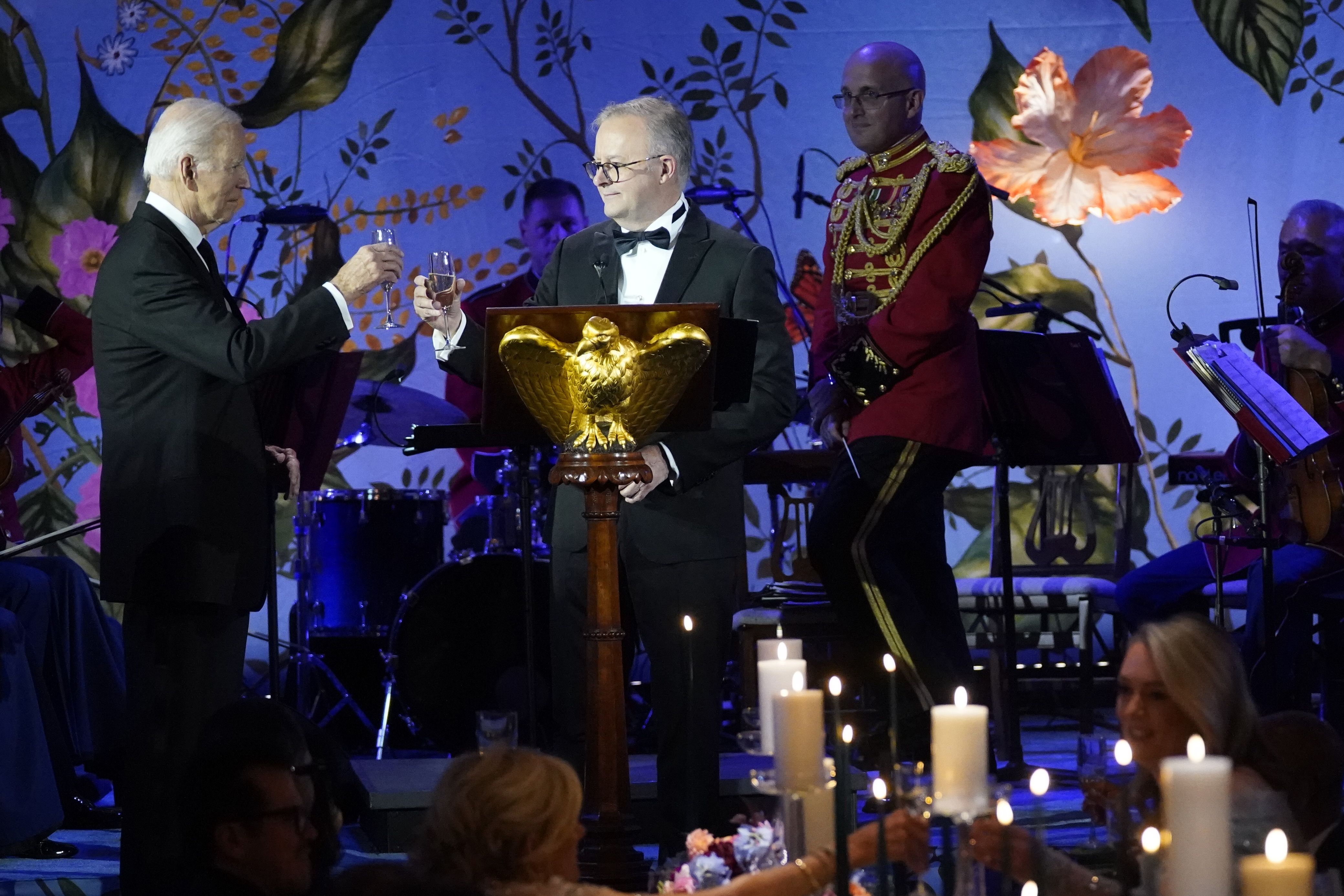 Biden and Albanese share a toast at the state dinner in Washington, DC. They are wearing evening dress. The room is bathed in a blue light.
