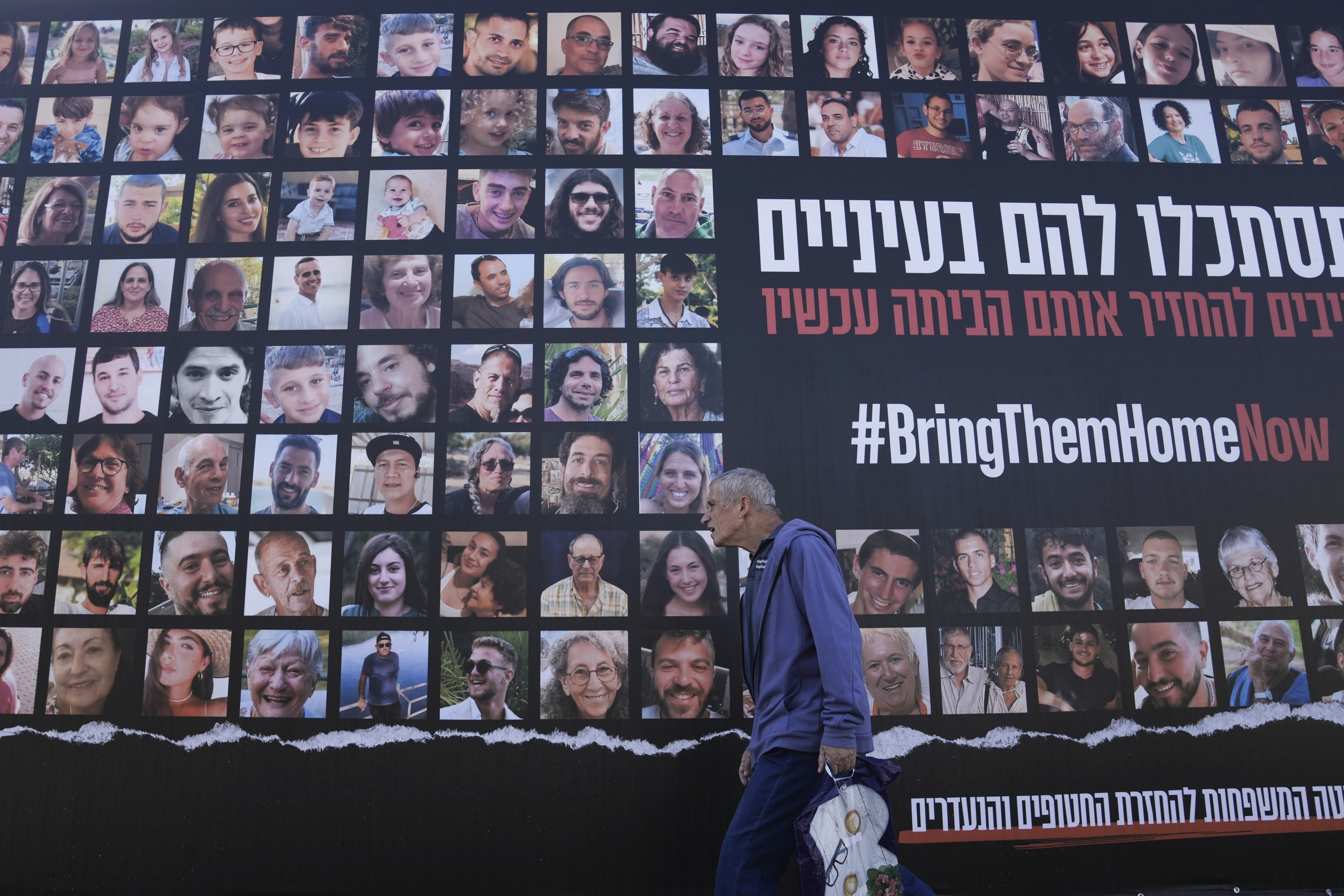 A man walks past a billboard calling for the return of about 240 hostages who were abducted during the Oct. 7, Hamas attack on Israel in Jerusalem on Friday.