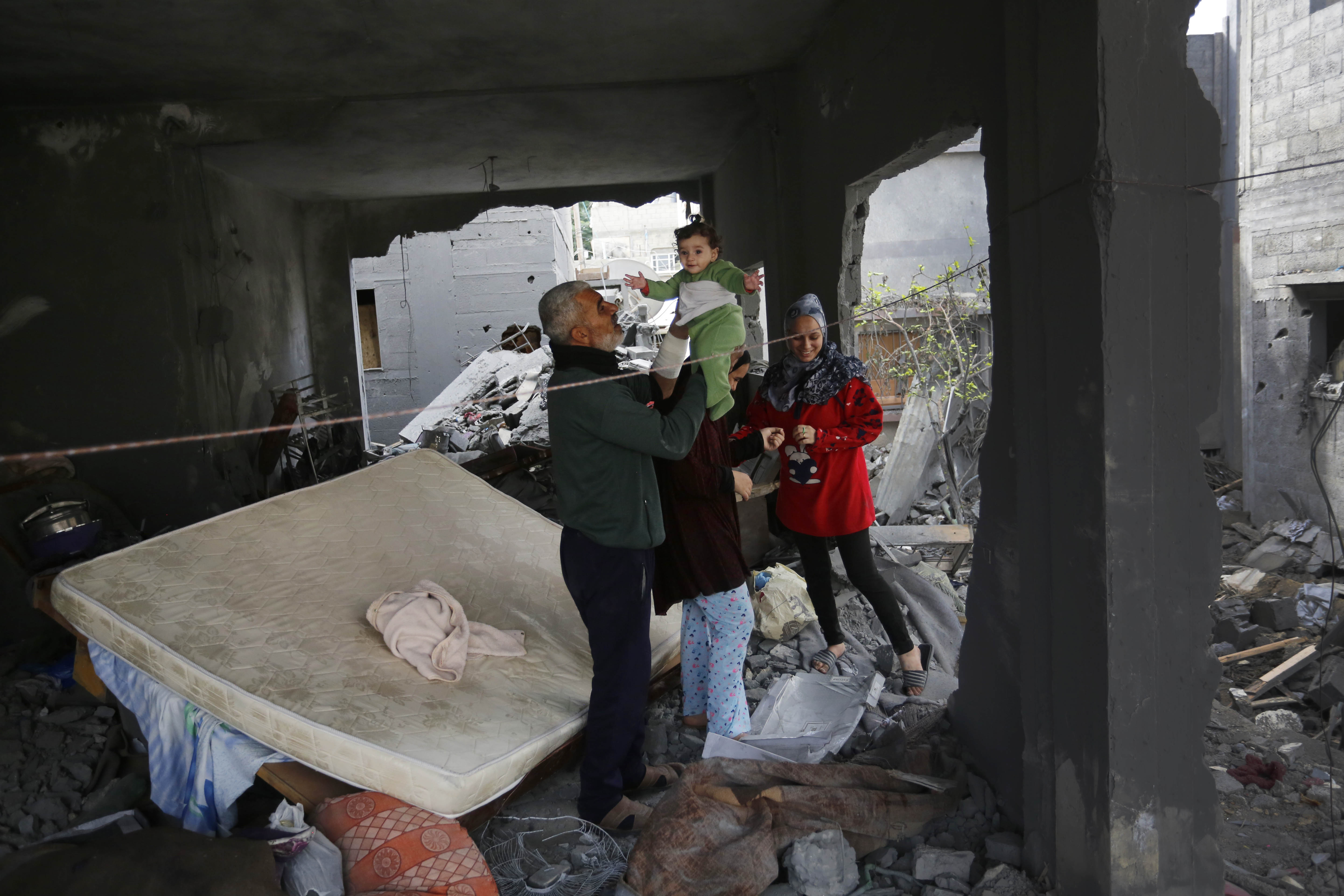 In the ruins of their home in Deir al-Balah, Khaled Naji plays with his granddaughter, Saida. His daughters Mona and Layan walk through the rubble [Ashraf Amra/Al Jazeera]