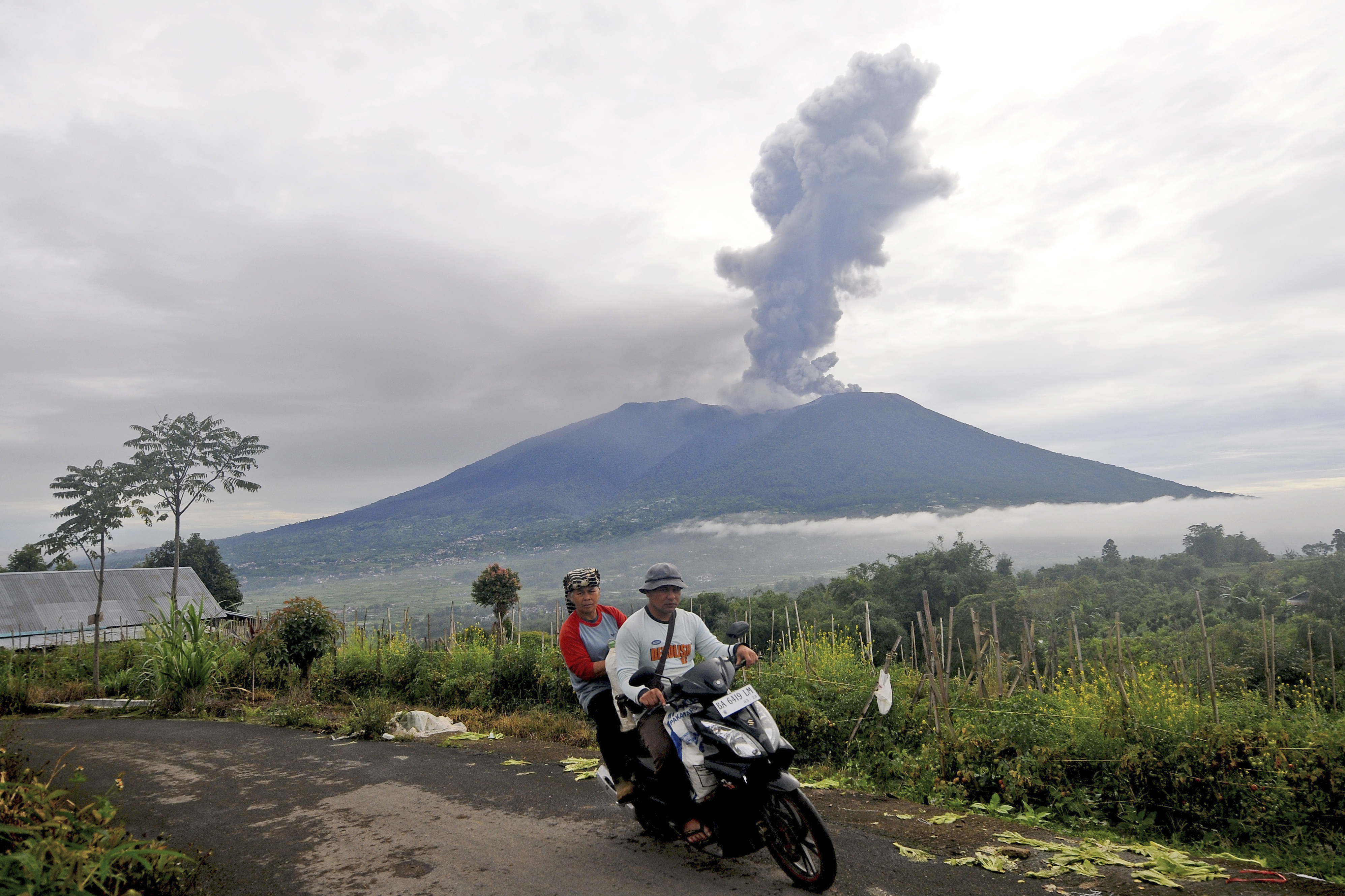 Motorists ride past by as Mount Marapi spews