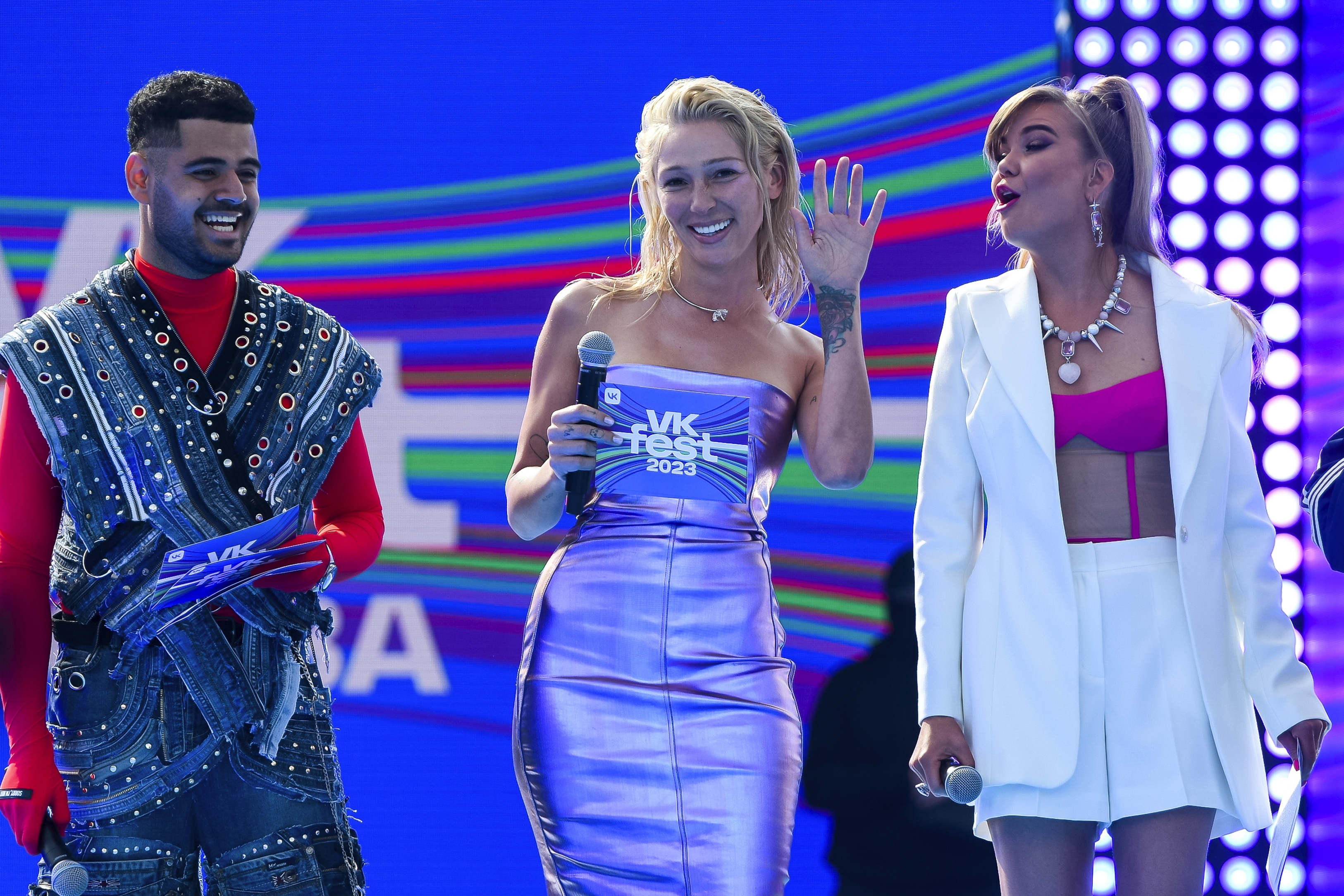 TV presenter and actress Anastasia Ivleeva pictured at an event in Moscow in July. She is wearing a metallic strapless dress and standing beside two other people on a stage.