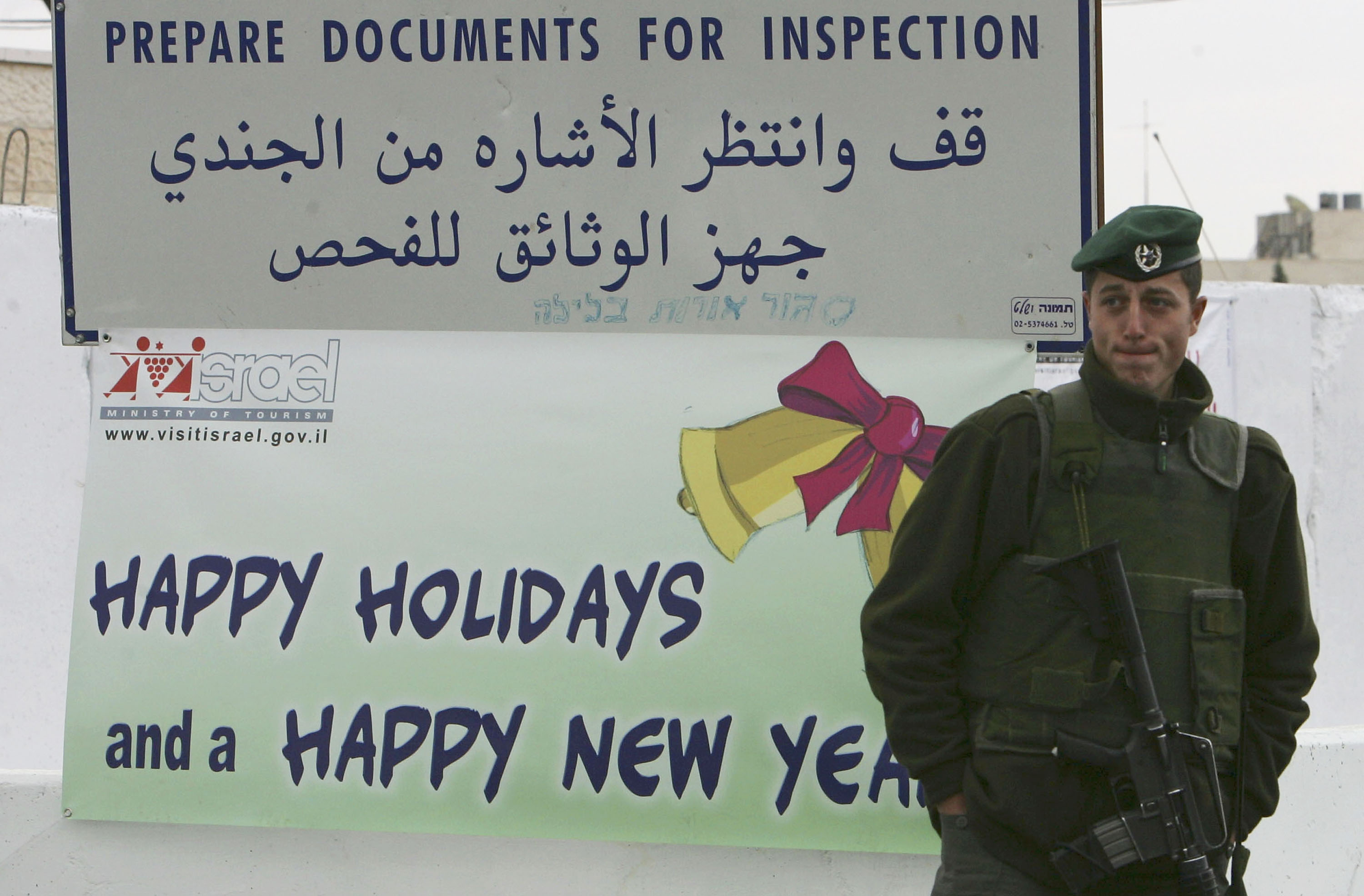 An Israeli border policeman stands guard on Christmas Eve December 24, 2004 at the checkpoint between Jerusalem and the West Bank town of Bethlehem where a sign welcomes visitors to the biblical town of Jesus's birth. The Israeli army says it is doing its utmost to promote the holiday spirit and that for the first time in more than a year, it has given Palestinian police in Bethlehem permission to carry weapons so that they can handle security inside the city. 
