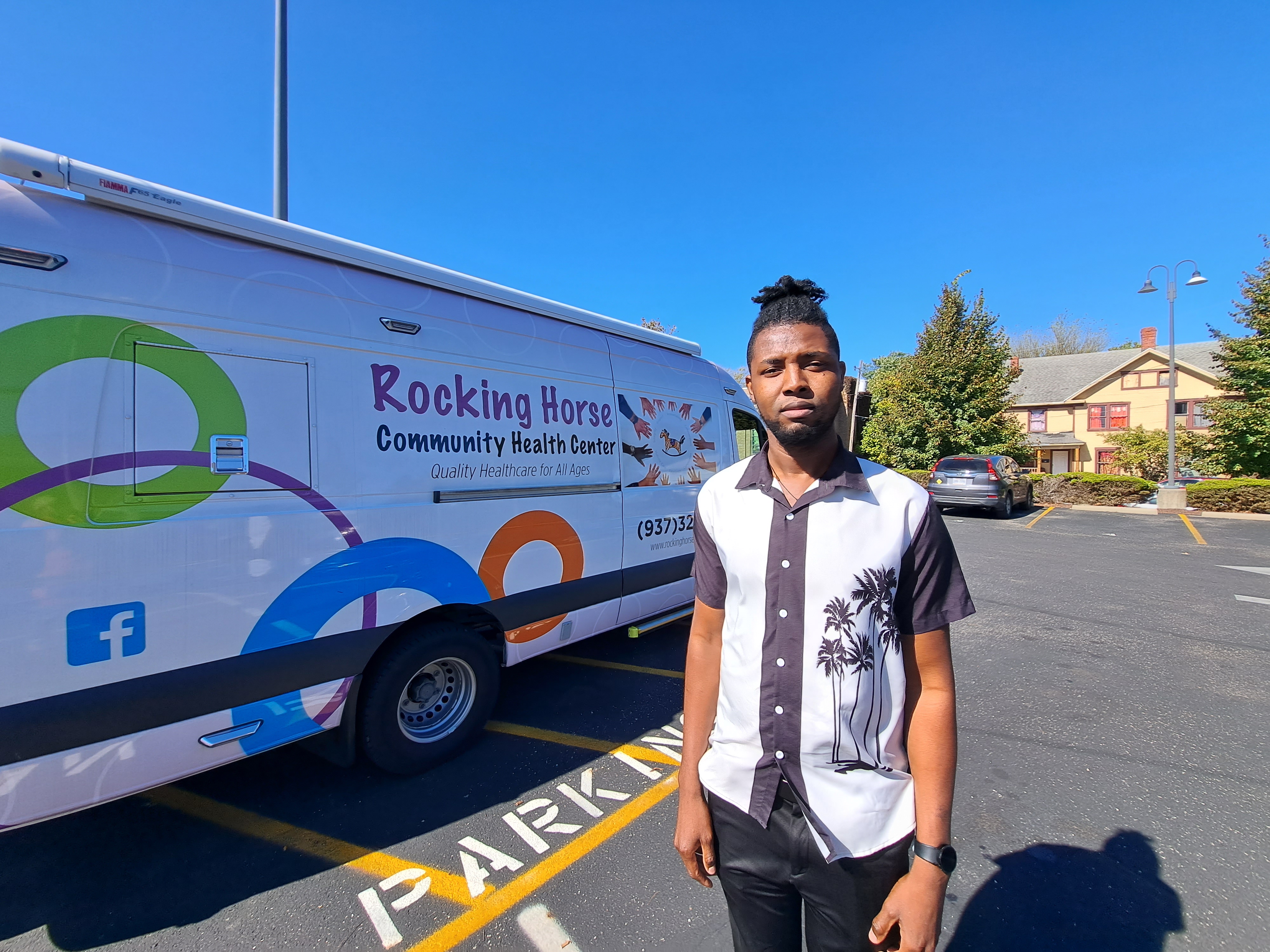 A man in a white-and-black collared shirt stands in front of a van for the Rocking Horse medical centre in Springfield, Ohio.