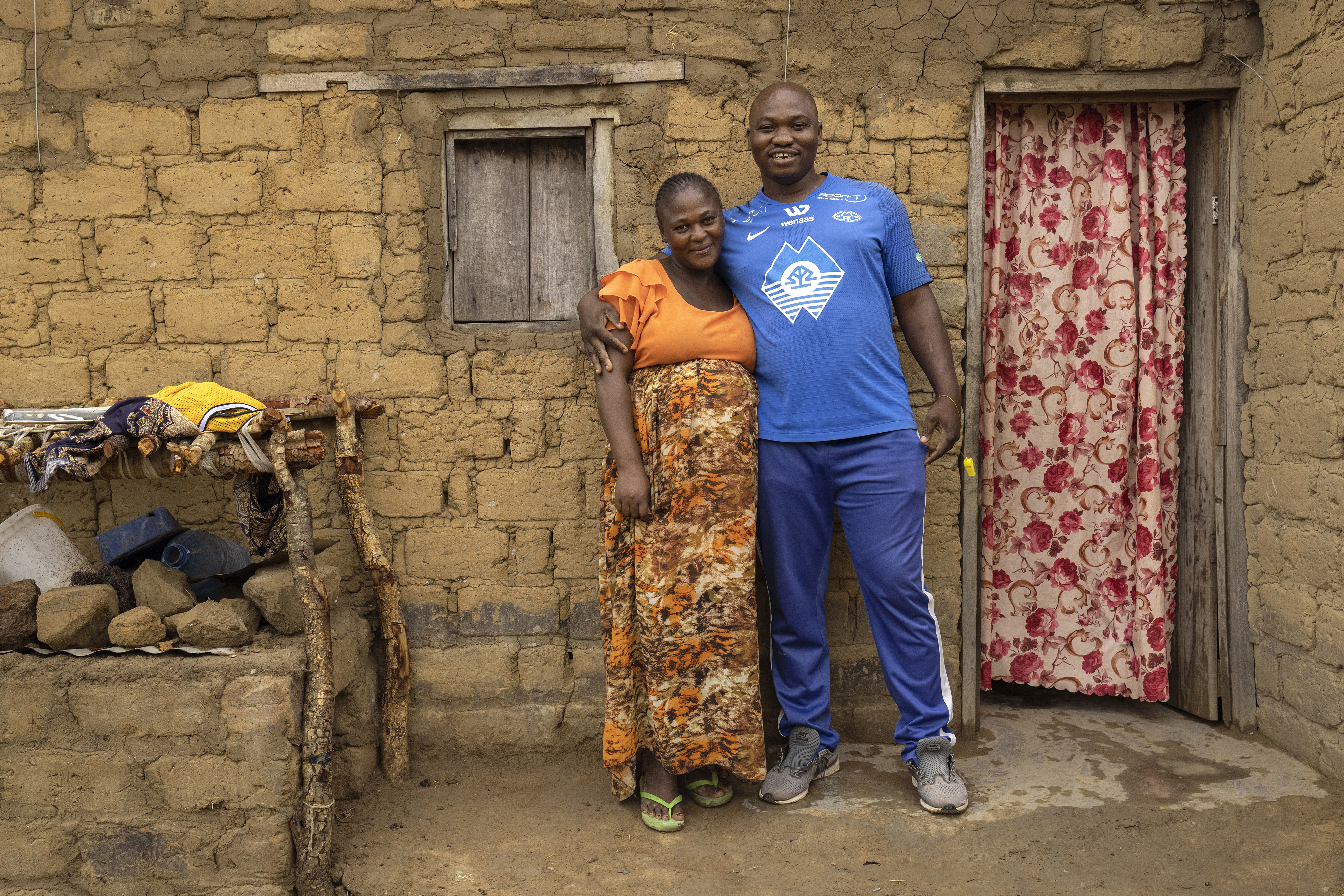 A man and his wife stand in front of their mudbrick home in a refugee camp in Zambia