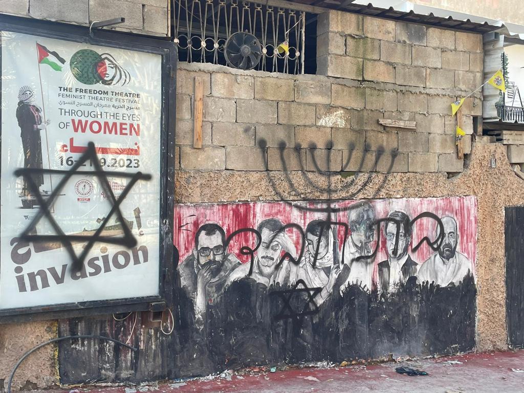 a Star of David is spray painted in black on a wall with a Palestinian flag