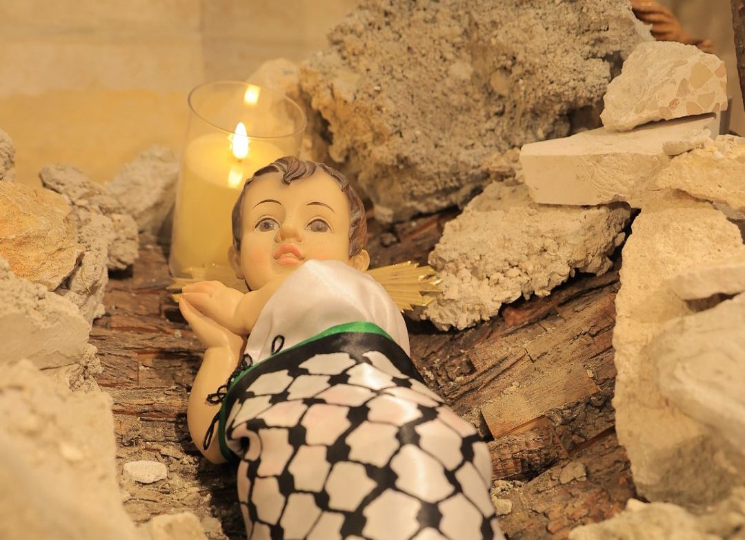 Closeup of Baby Jesus doll wrapped in Palestinian keffiyeh in the rubble manger