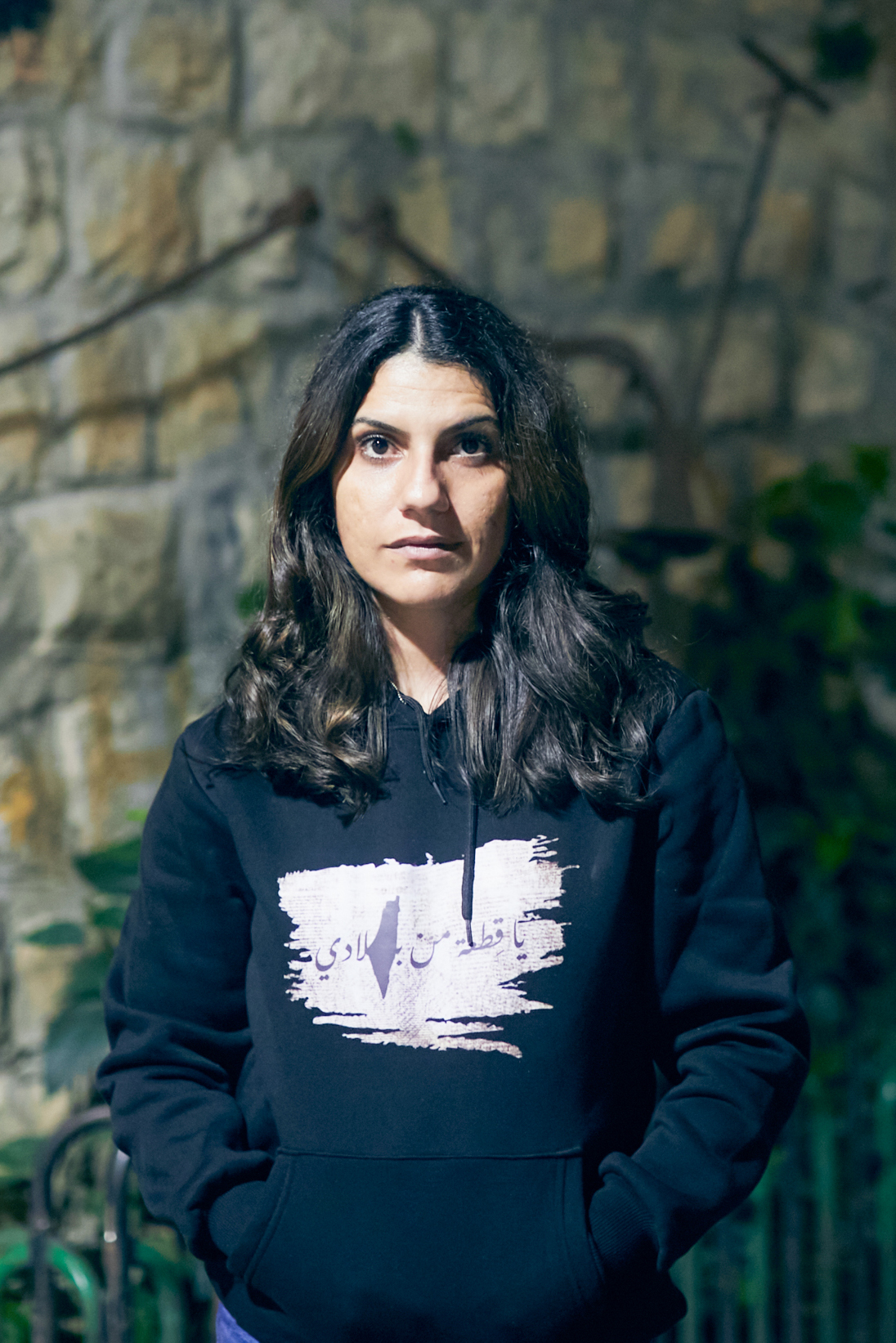 Nour in dark sweatshirt standing in a sone house