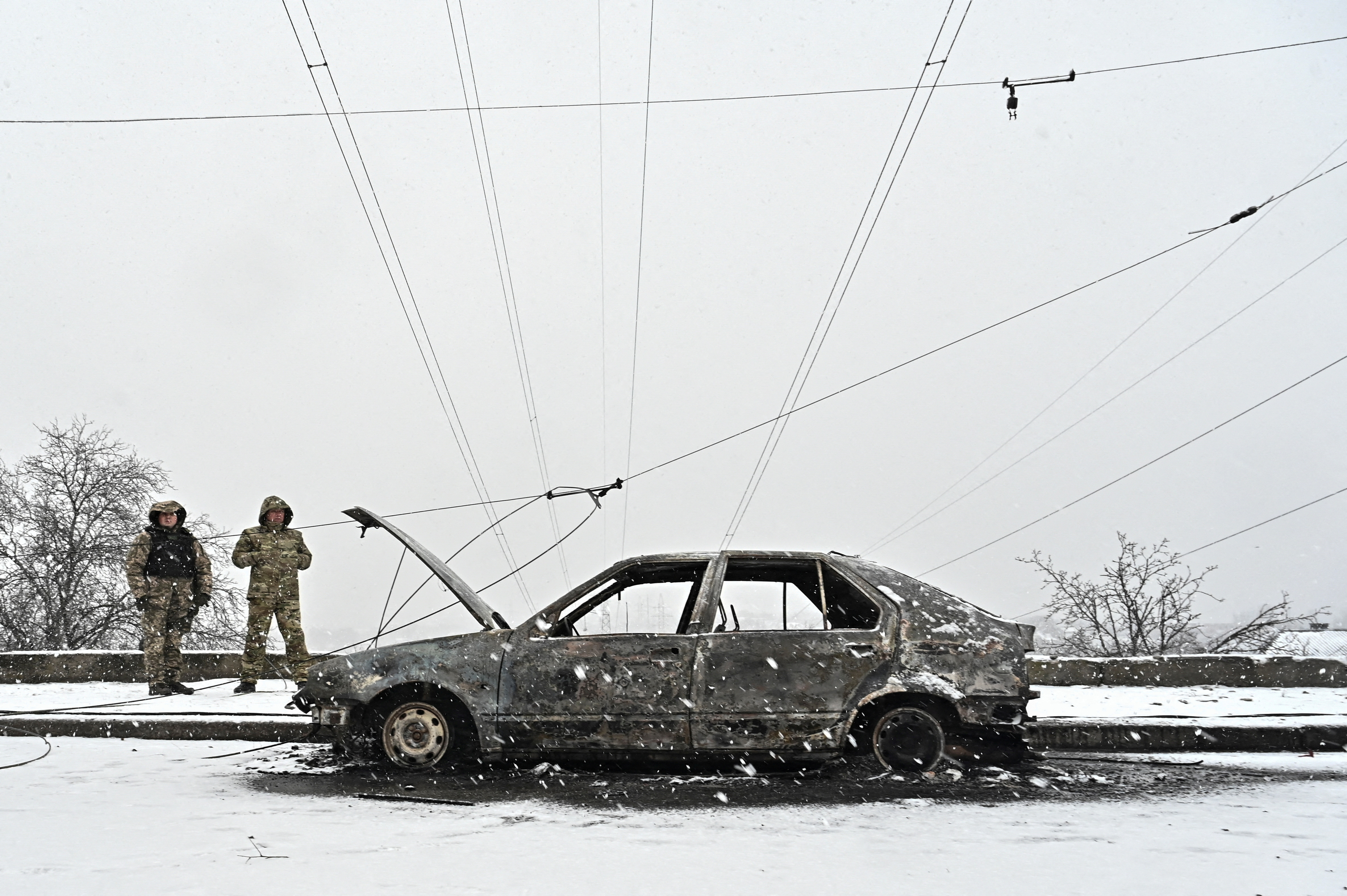 A car destroyed in a Russian missile strike on Zaporizhia. Two investigators are standing nearby. It's snowy