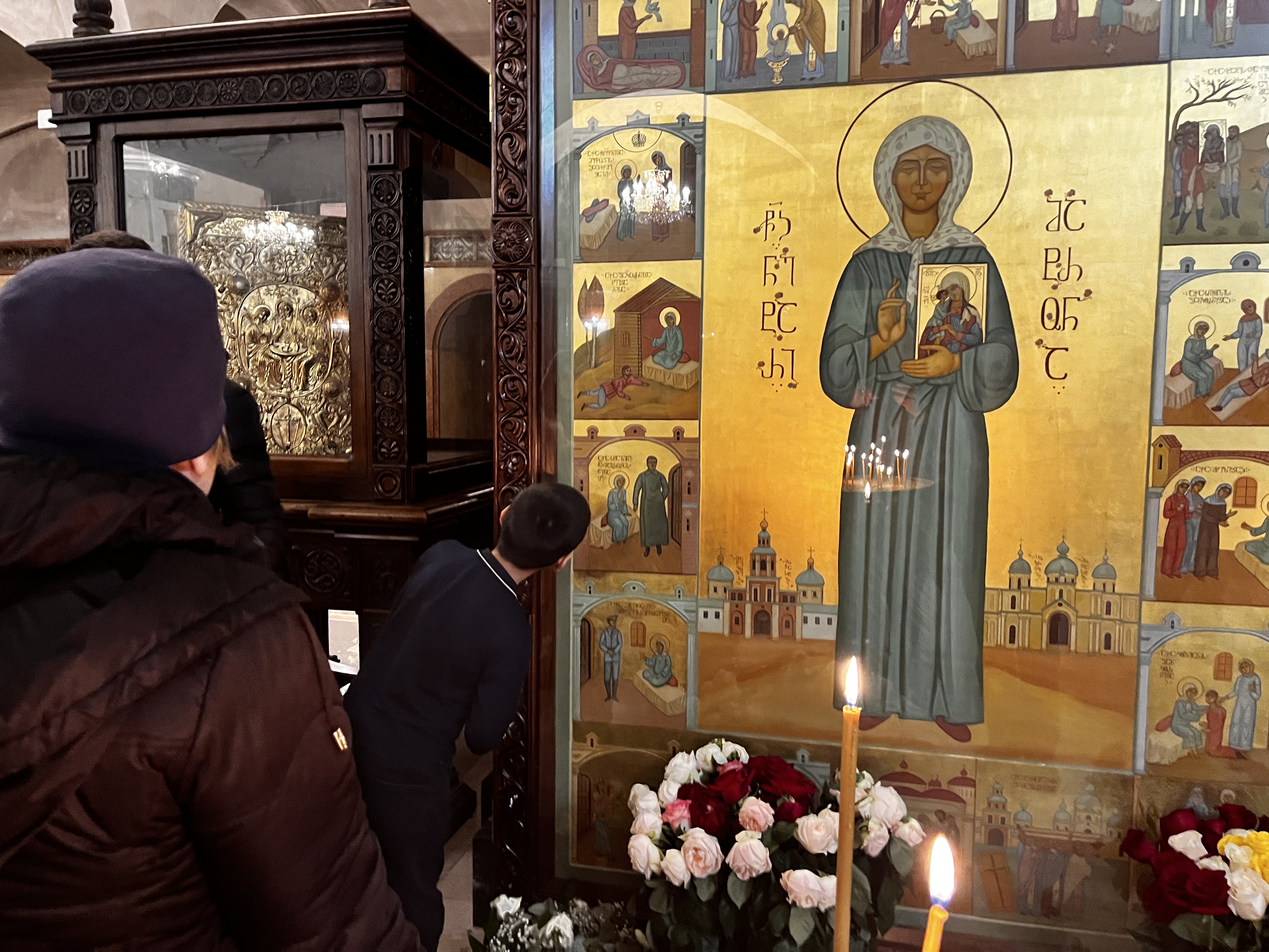 A boy leans forward to kiss the icon of Saint Matrona featuring Stalin inside Tbilisi's Sameba Cathedral [Al Jazeera]