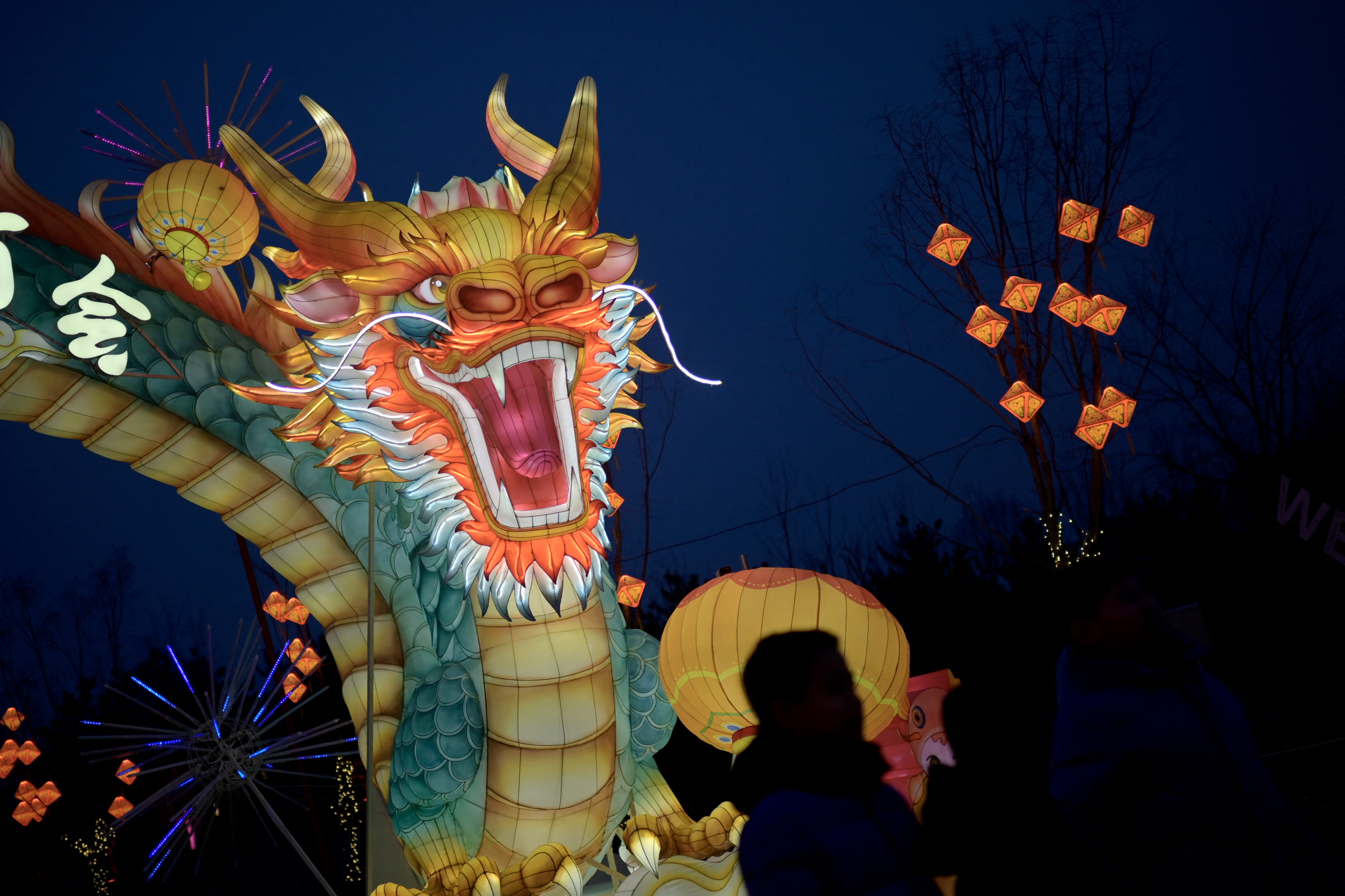 A dragon lantern lit up at night. People are walking nearby.