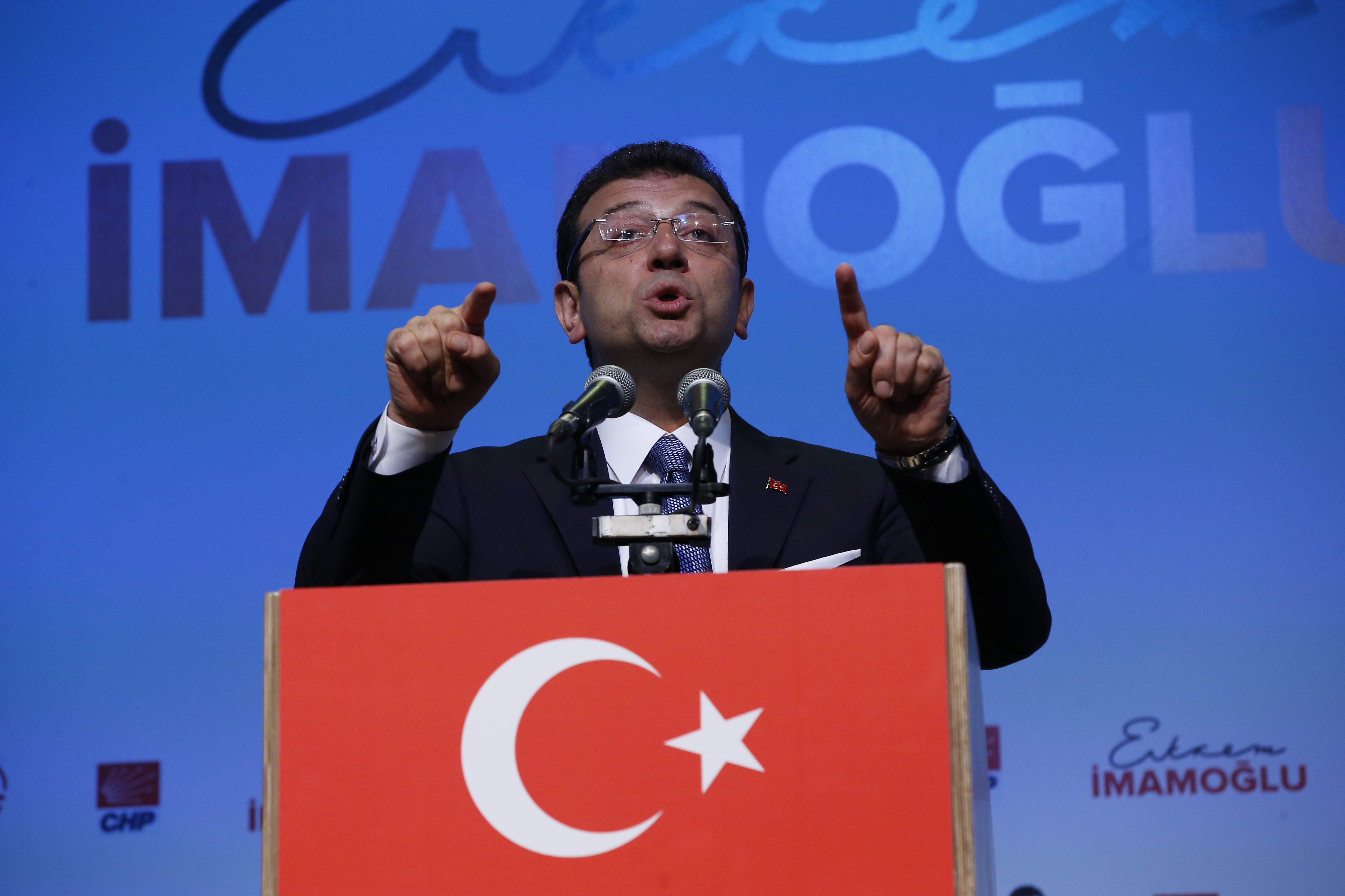 Ekrem Imamoglu gestures as he delivers a speech against a blue background