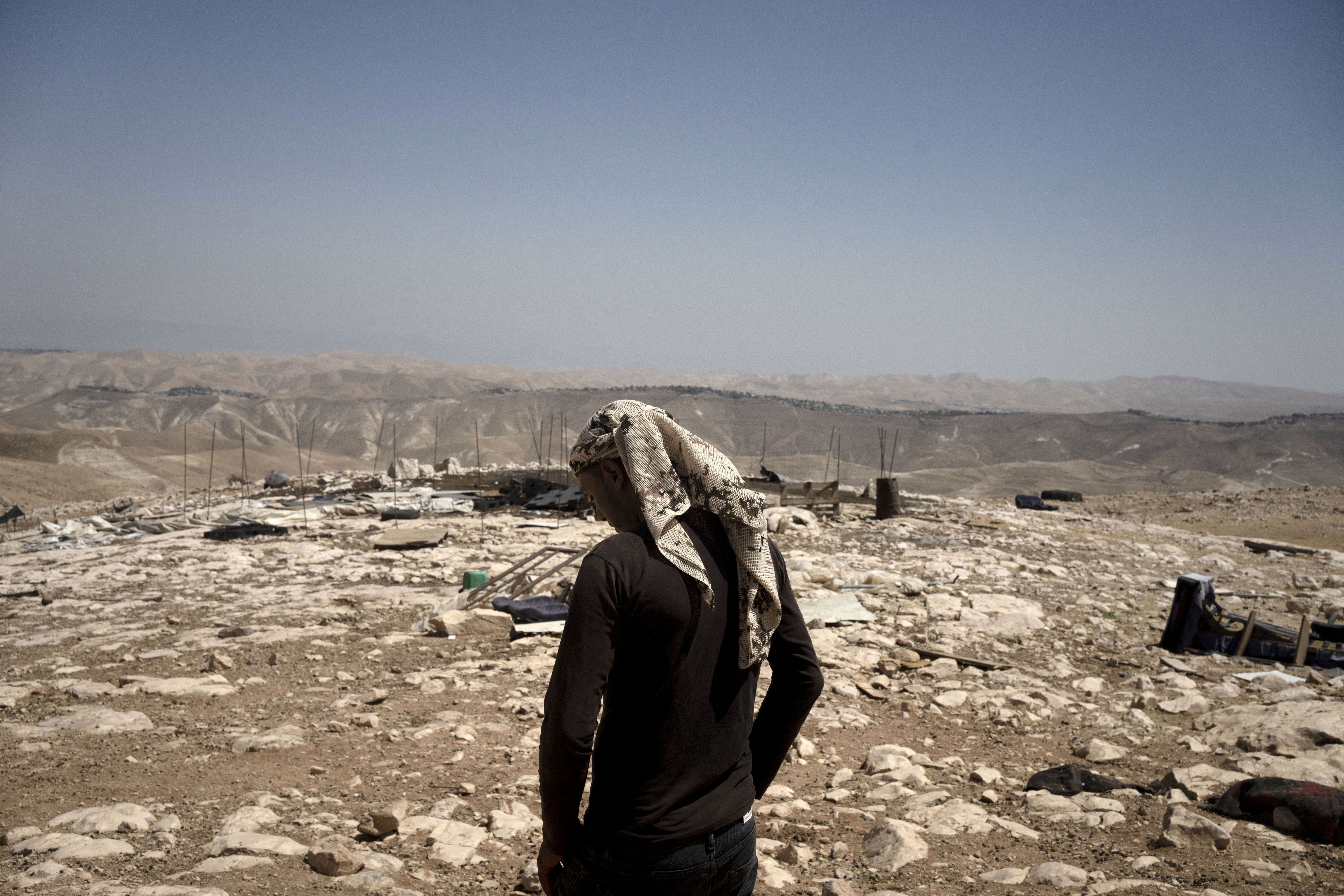 a woman wearing a sand coloured head scarf stands looking out onto a sandy landscape