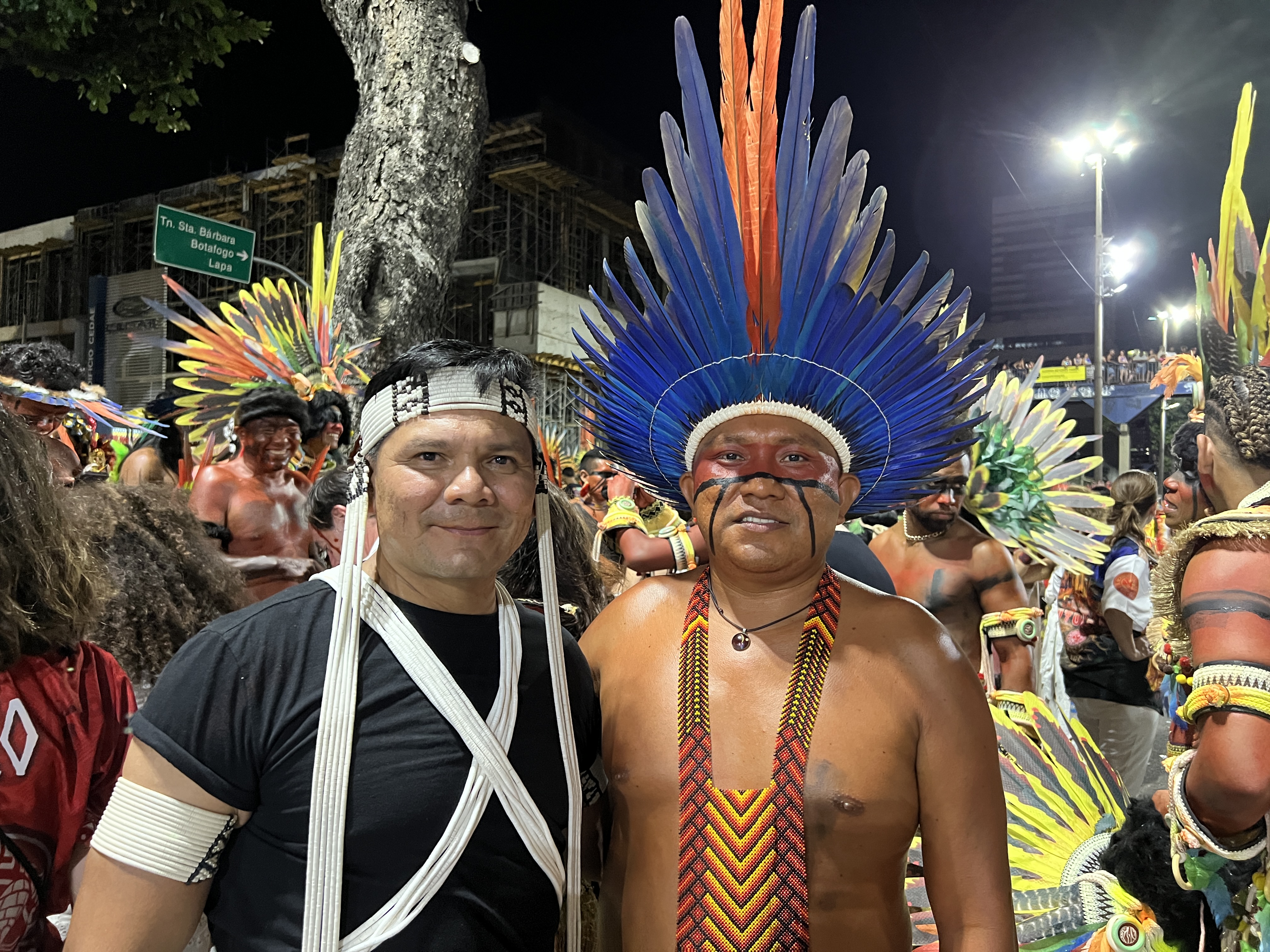 Two Indigenous activists — Dario Kopenawa and Beto Marubo — pose for a photo beneath Rio de Janeiro's night sky, as they prepare for a Sambadrome parade.