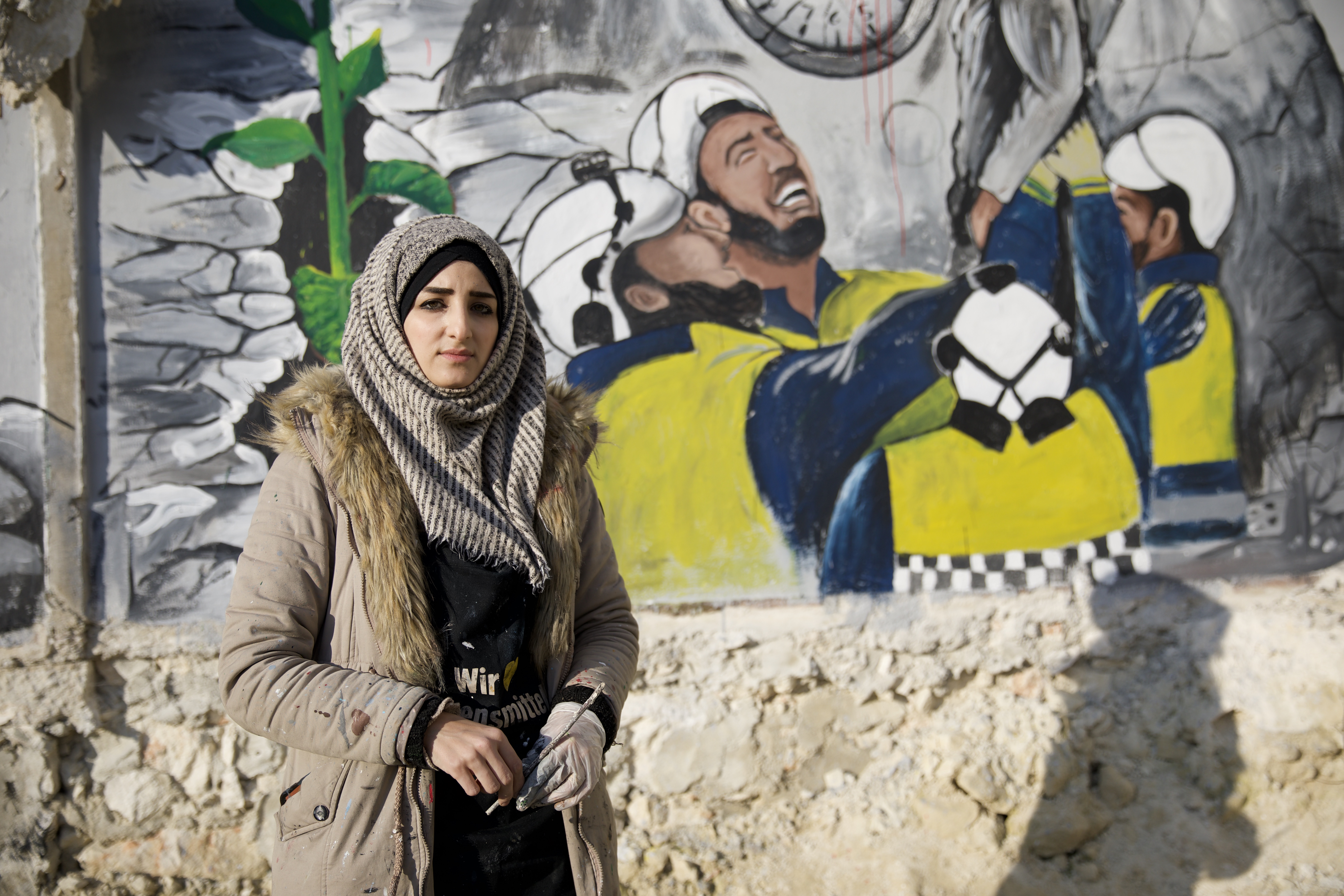Salam Al-Hamid, a graffiti artist, draws members of the Civil Defense rescuing a girl from under the rubble of the earthquake on a destroyed wall in the town of Al-Malind in the Idlib countryside