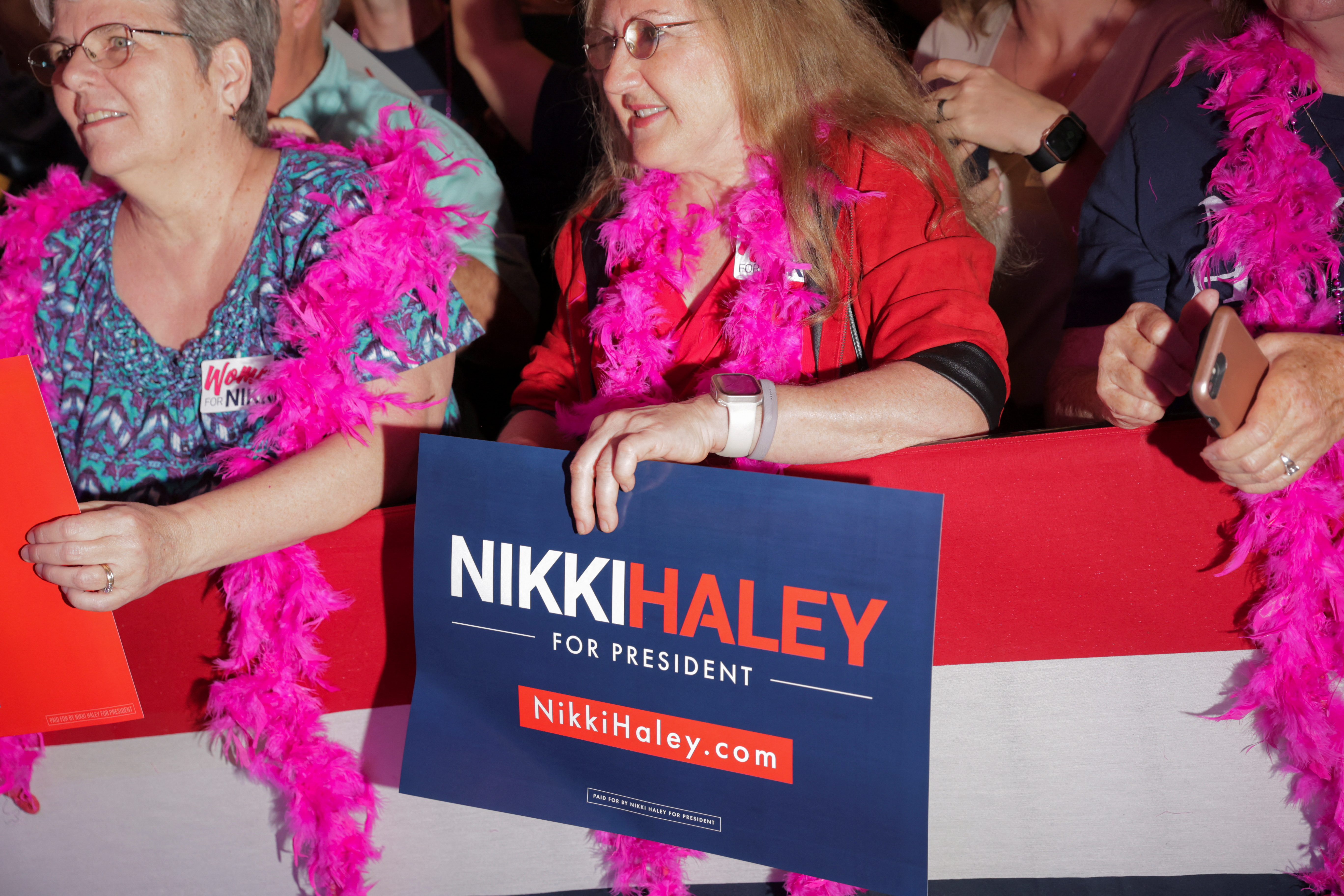A Nikki Haley supporter wears a feather boa and holds a sign in support of the candidate.