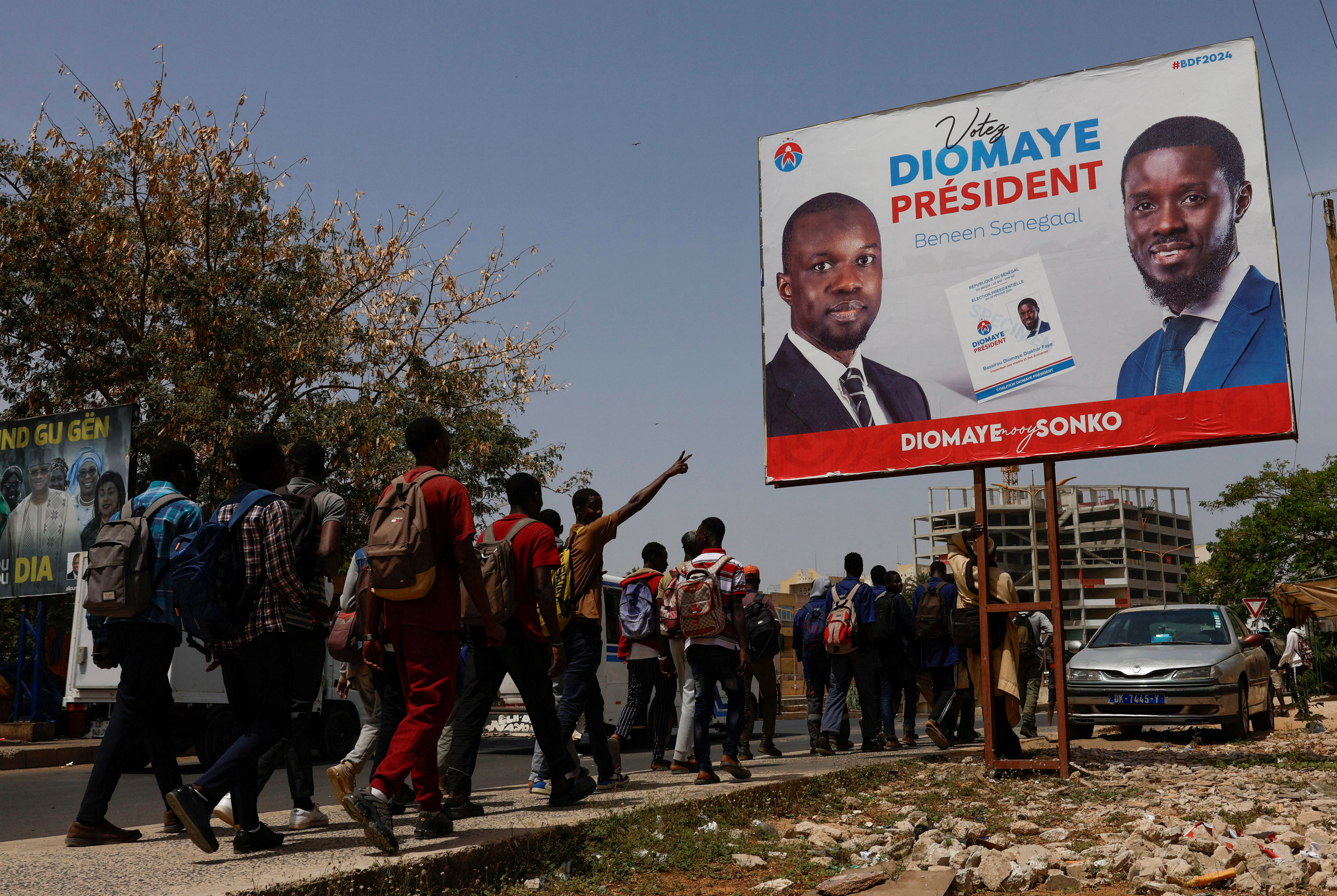 Students walks as they pass an electoral billboard of the Senegalese presidential candidate Bassirou Diomaye Faye, who is backed in the March 24 election by opposition leader Ousmane Sonko, in Dakar, Senegal, March 20, 2024