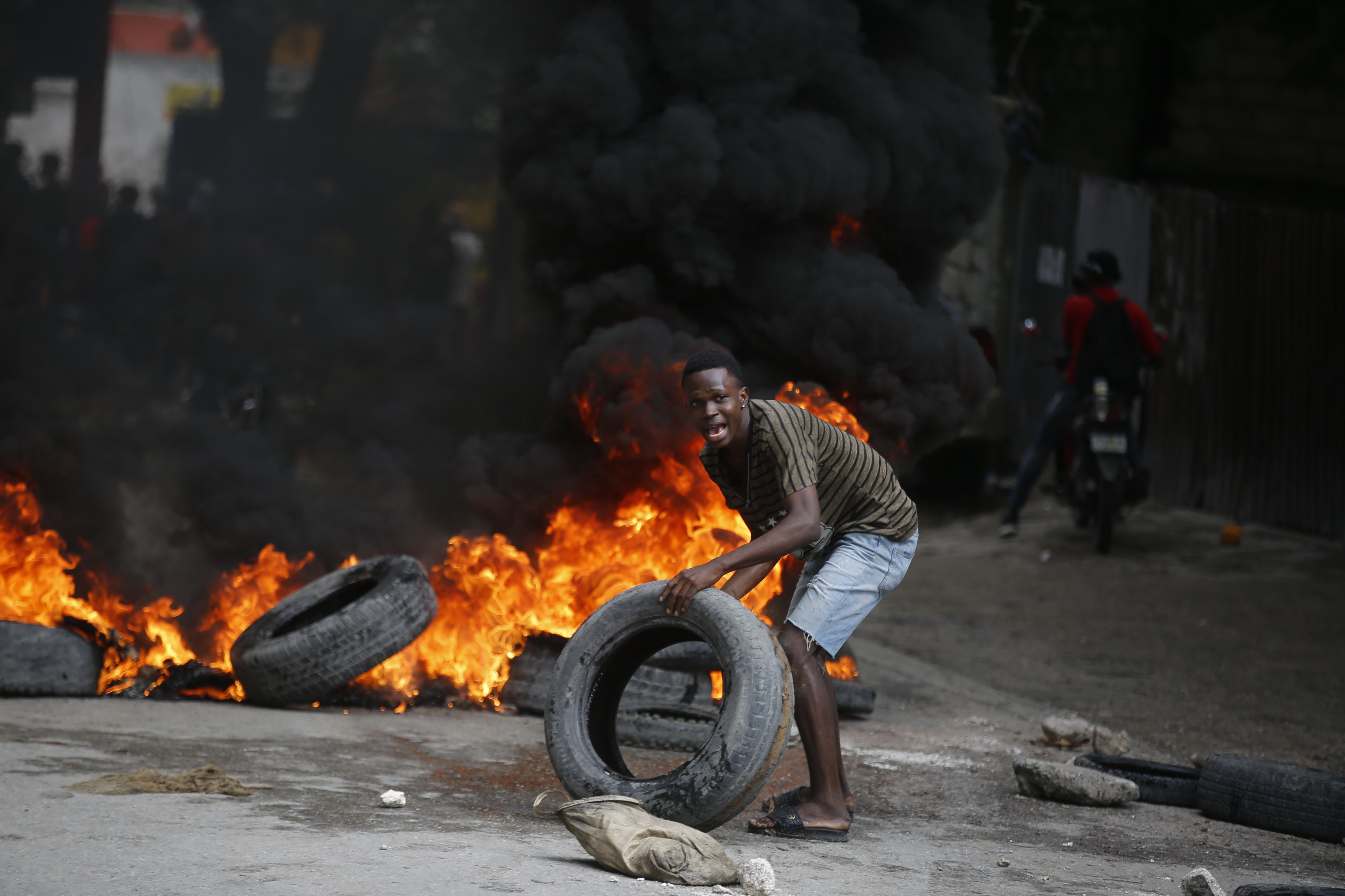 A protester adds tires to a burning barricade during a demonstration demanding the resignation of Prime Minister Ariel Henry