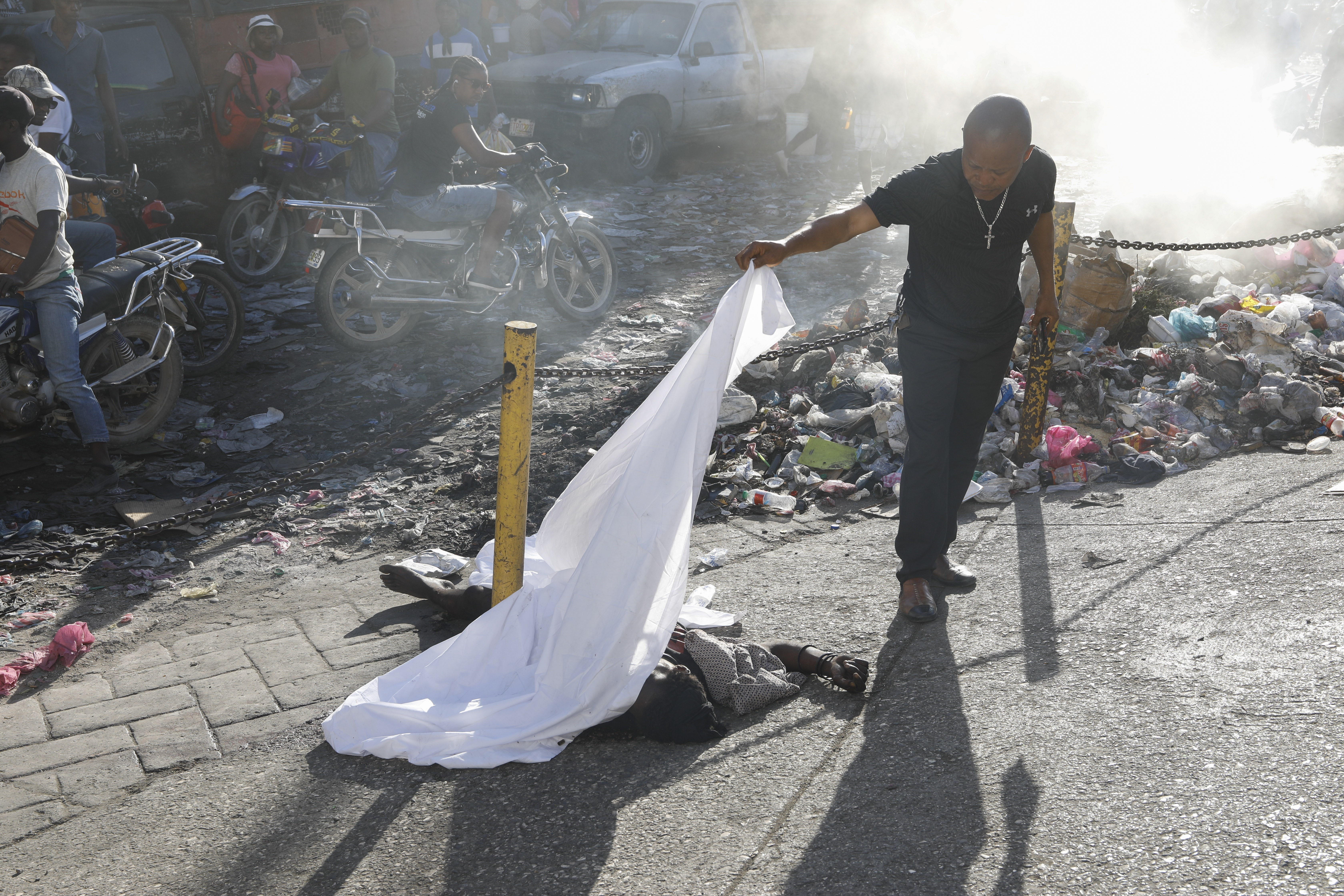 A person lifts a sheet to look at the identity of a body lying on the ground after an overnight shooting in the Petion Ville neighborhood