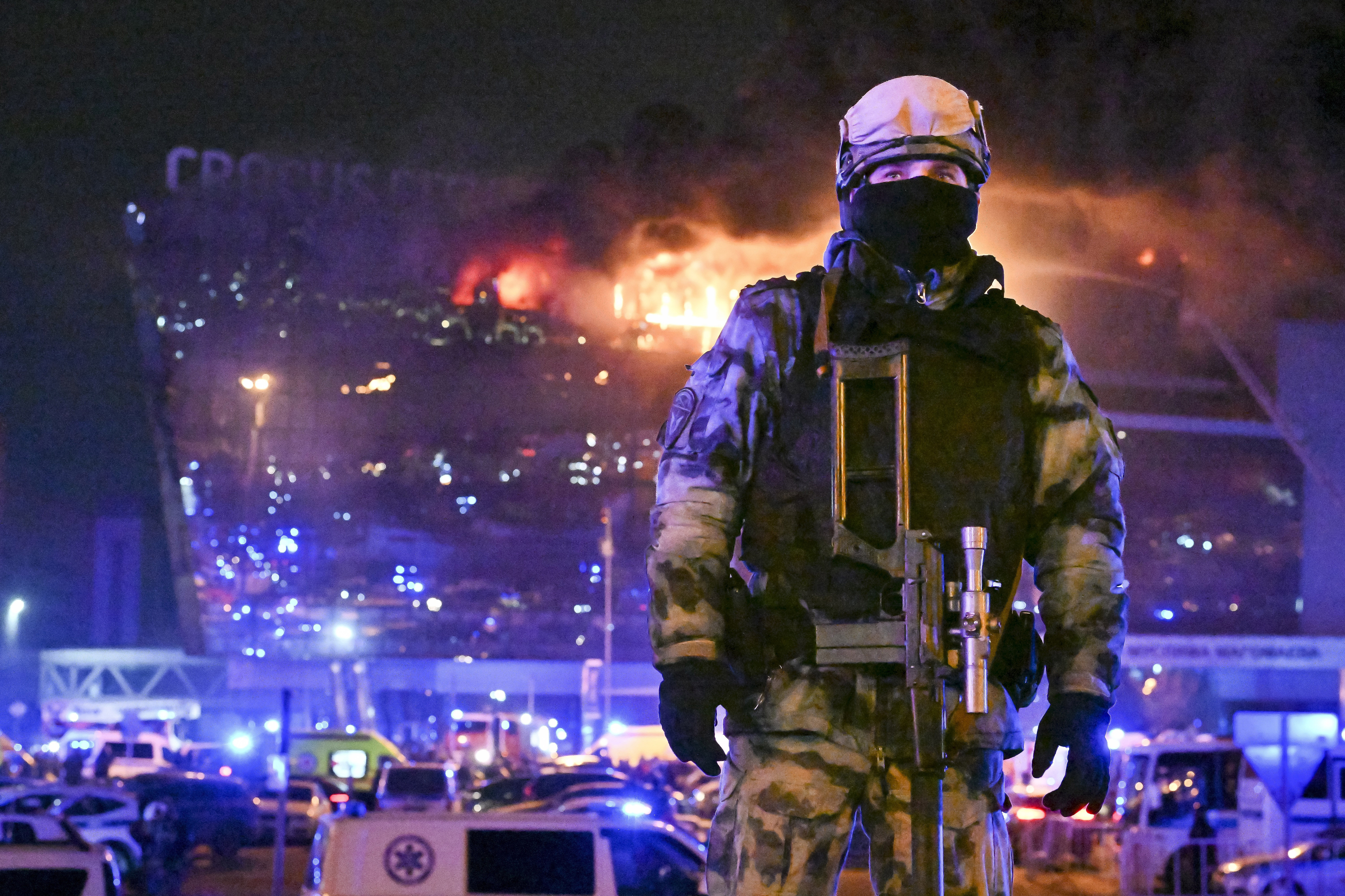 A member of Russia's national guard at the Crocus Concert Hall. The building is behind him in flames.
