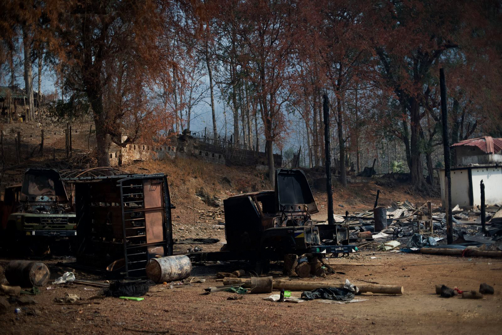 Destruction in Shadaw. Vehicles have been burned out and buildings left in ruins. Trees are behind