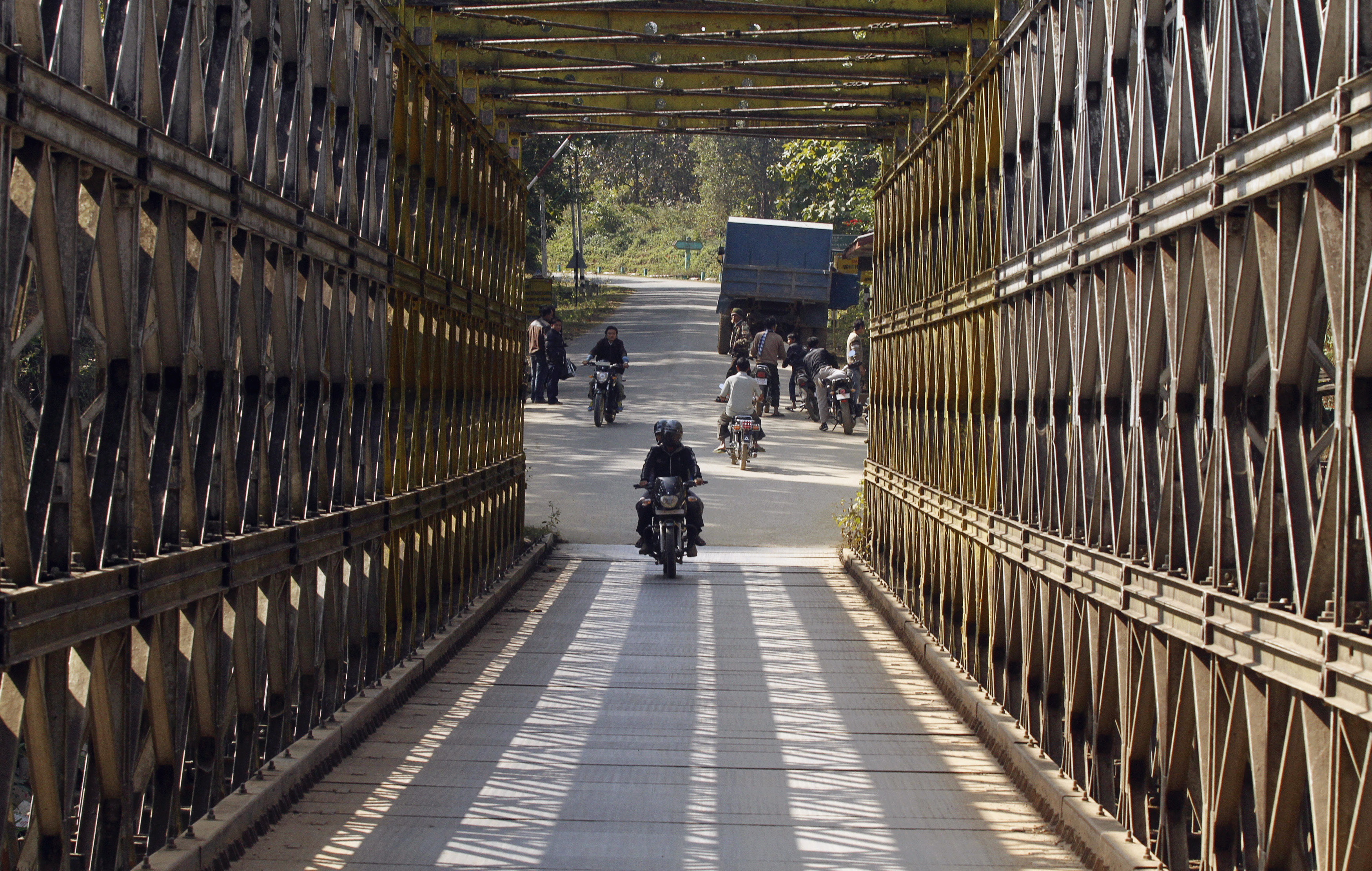 People ride motorbikes as they cross a border bridge.