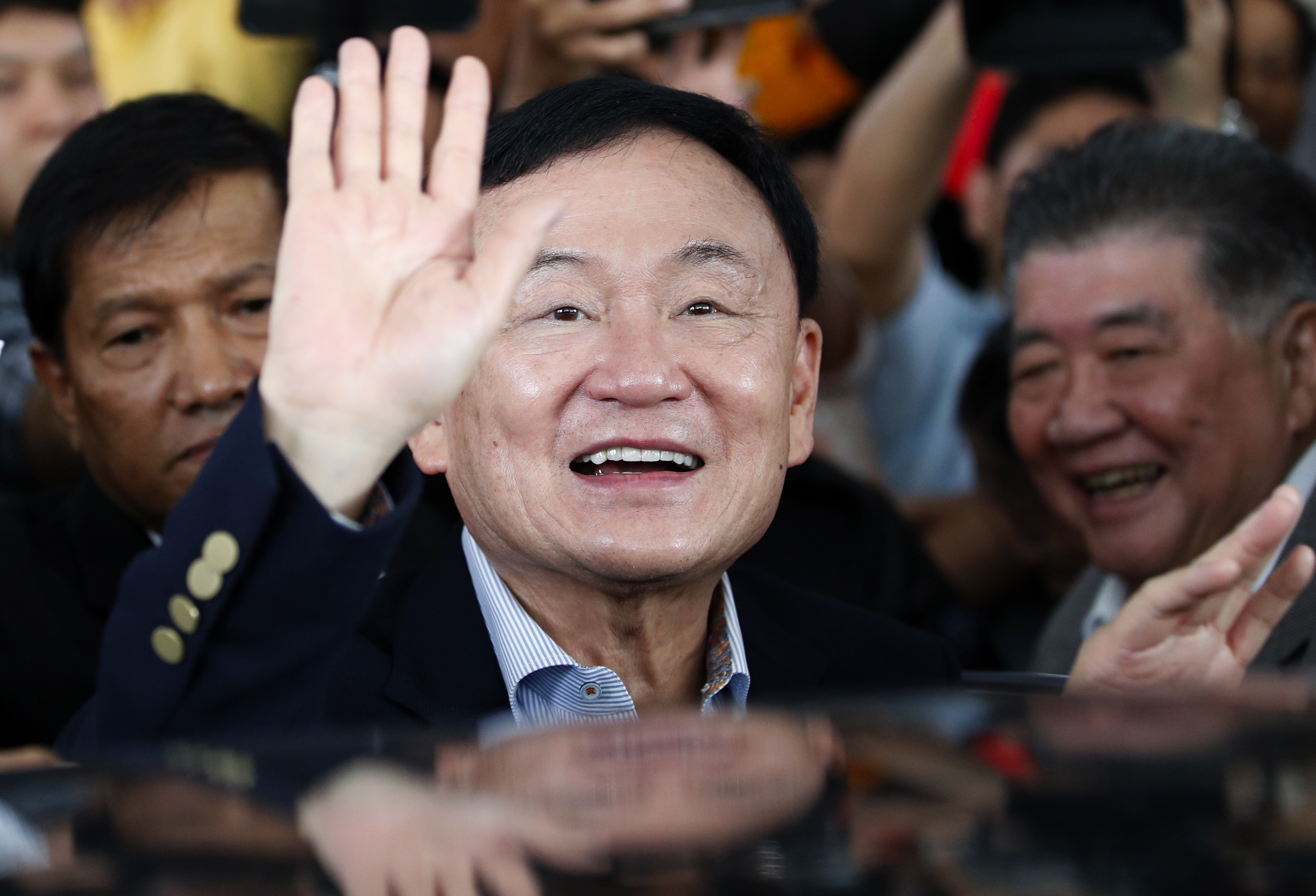 Thaksin Shinwatra waving. He is surrounded by supporters.