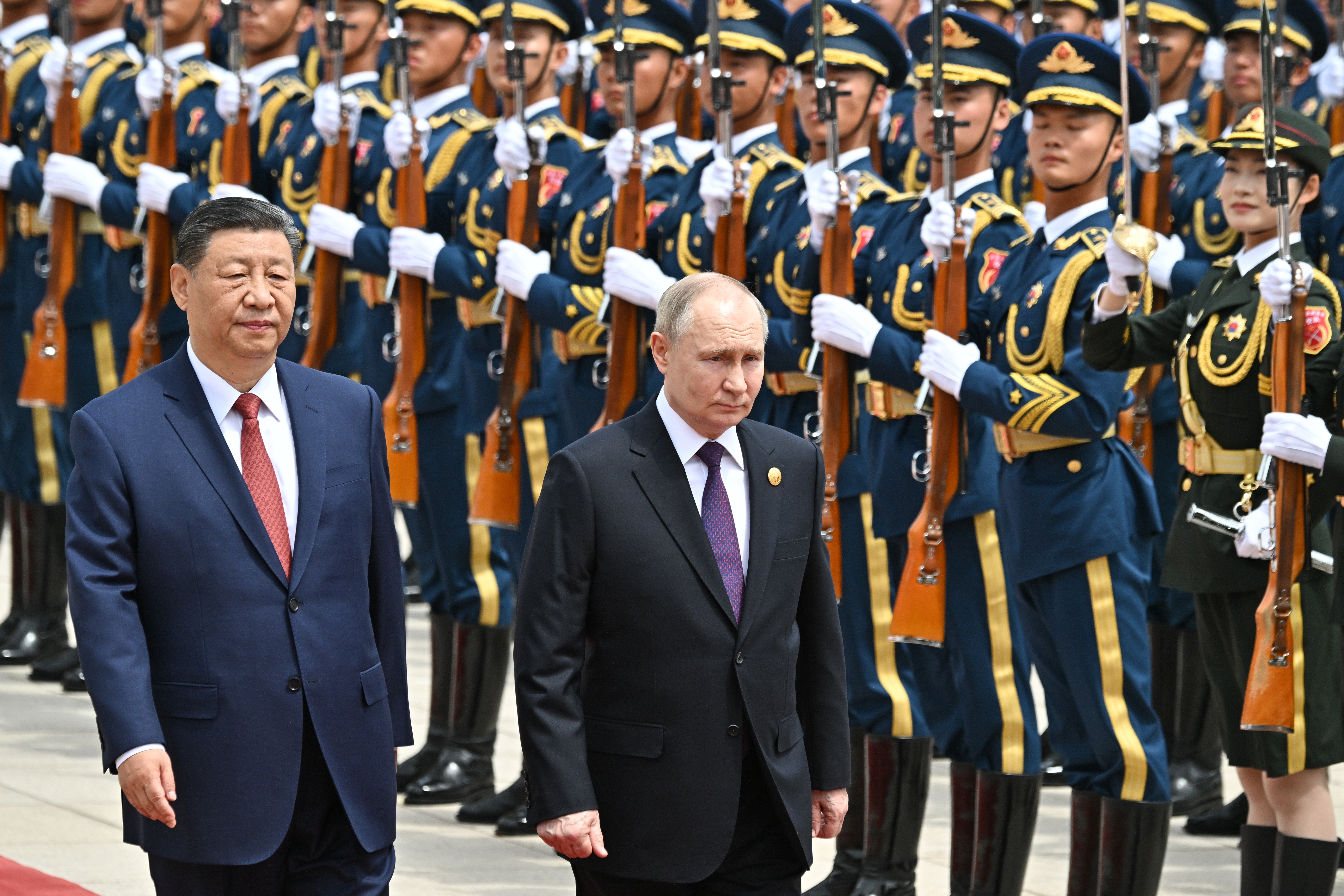 Xi Jinping and Vladimir Putin walking in front of massed troops in Beijing. Putin is nearest the soldiers. The troops are standing to attention.
