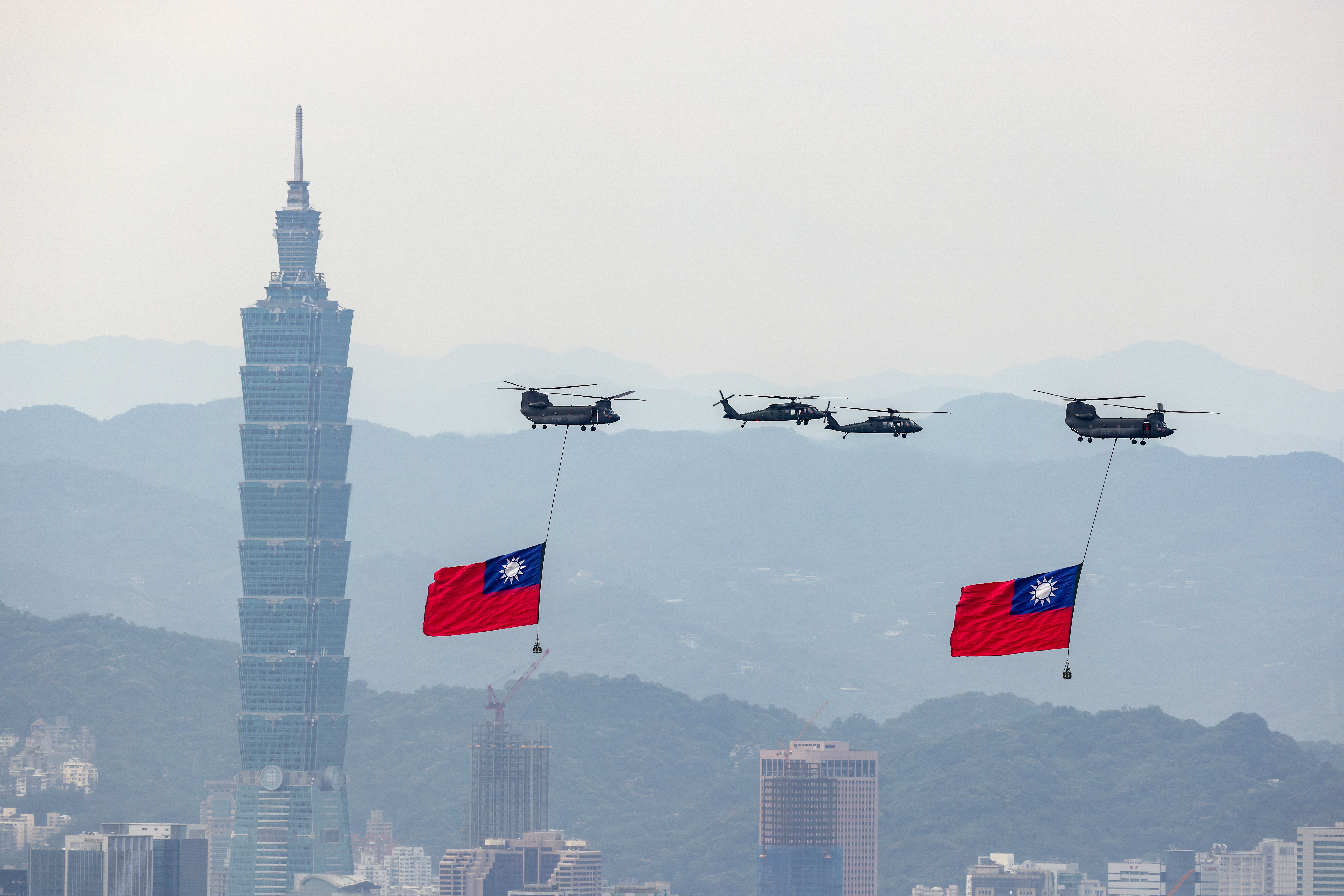 Helicopters carrying Taiwan's national flags in the sky above Taipei. Taipei 101 is behind them.