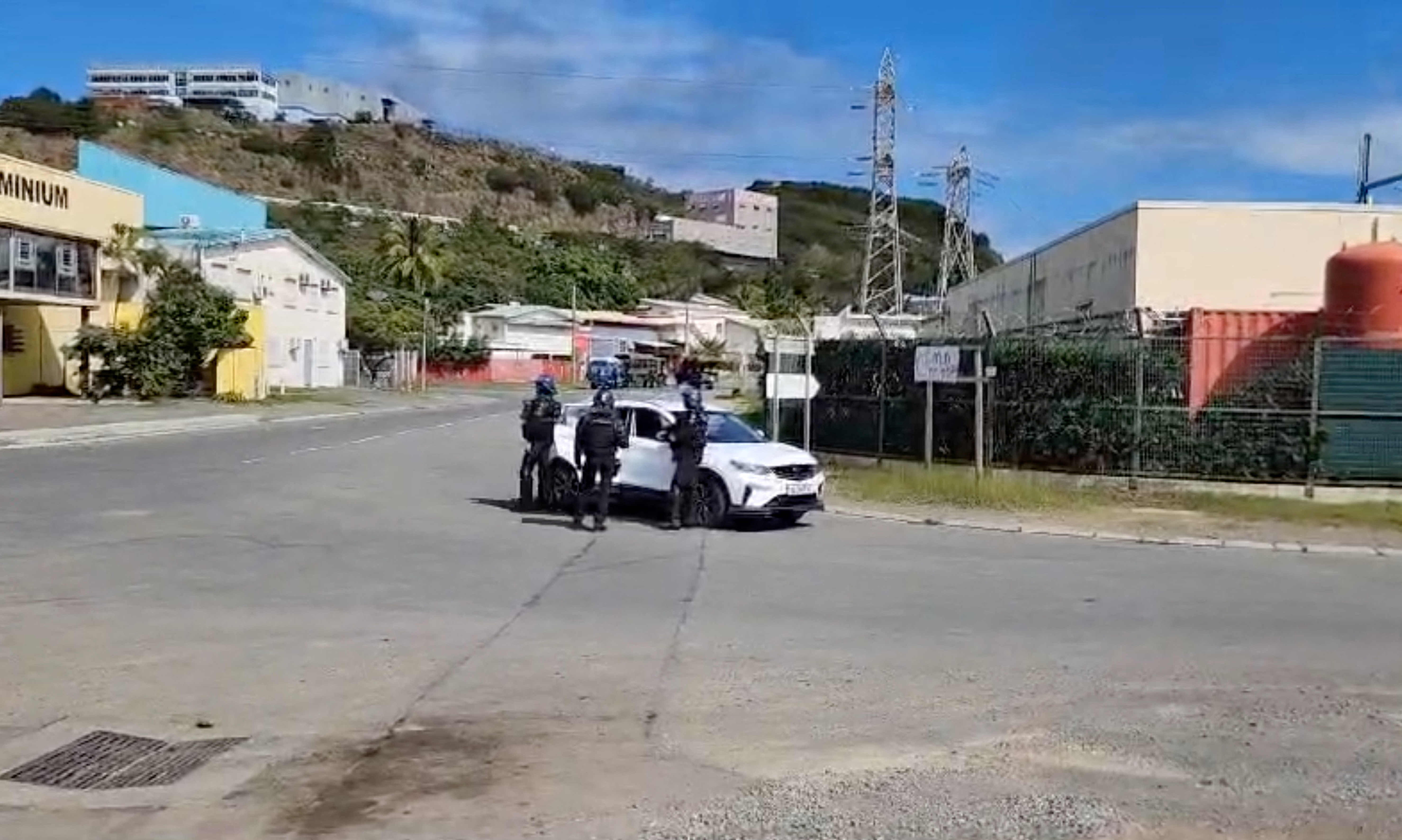 Police at a deserted road junction in Noumea. There are buildings around them. The road has been scorched by fire