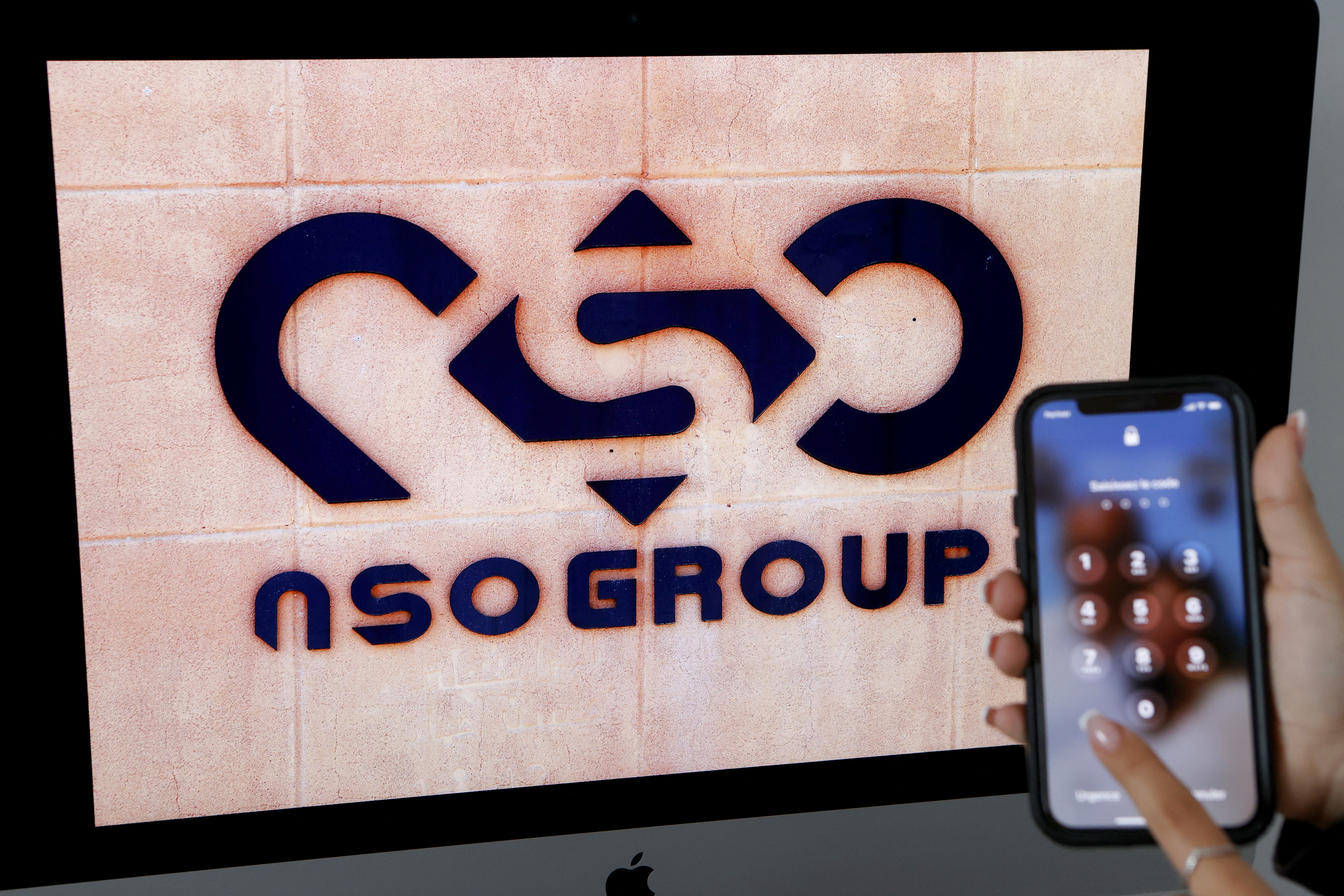 A photographic illustration shows a mobile phone near the NSO Group company logo on February 9, 2022 in the Israeli city of Netanya. Israel's ground-breaking surveillance technology was once feted as a prized export bolstering diplomatic ties abroad, but reports the secret spyware was also turned on citizens at home has trigged domestic outrage. Recent bombshell allegations in Israeli media centre on the controversial Pegasus malware made by the Israeli firm NSO, which can turn a phone into a pocket spying device. (Photo by JACK GUEZ / AFP)