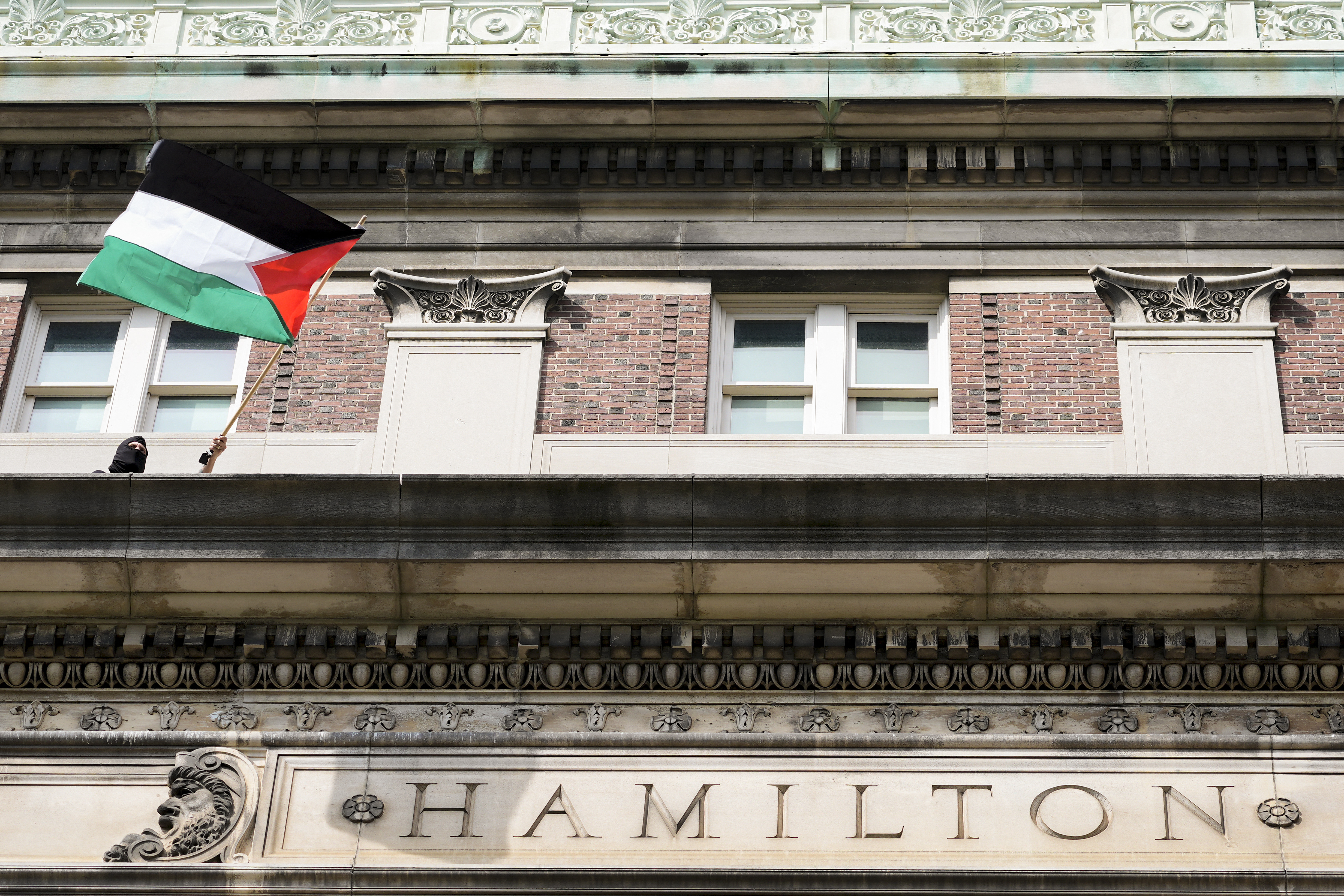 A pro-Palestinian student protester waves a Palestinian flag from a balcony of Hamilton Hall