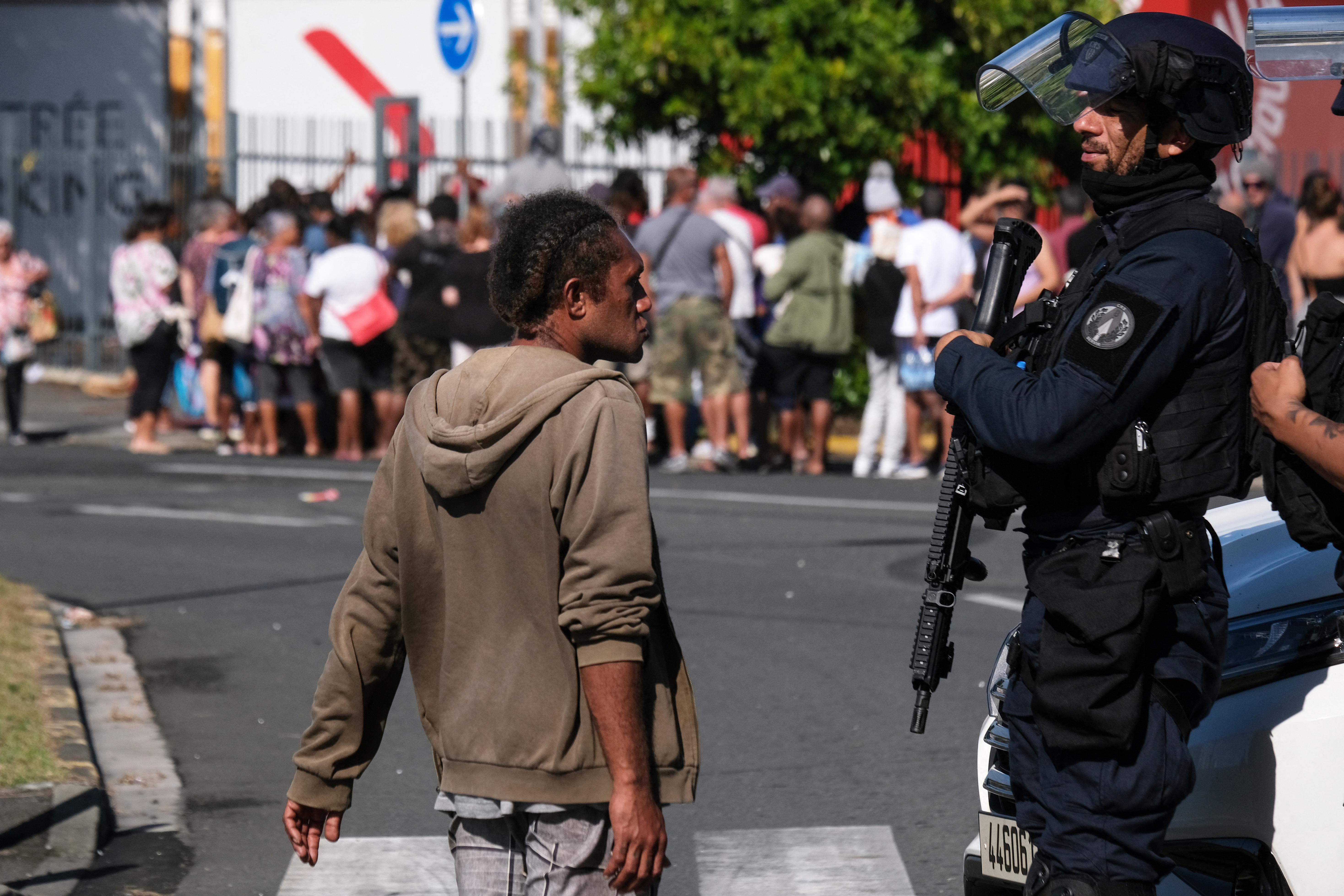 A police officer interacts with a man as others queue to enter a supermarket in the Magenta district of Noumea, France's Pacific territory of New Caledonia, on May 18