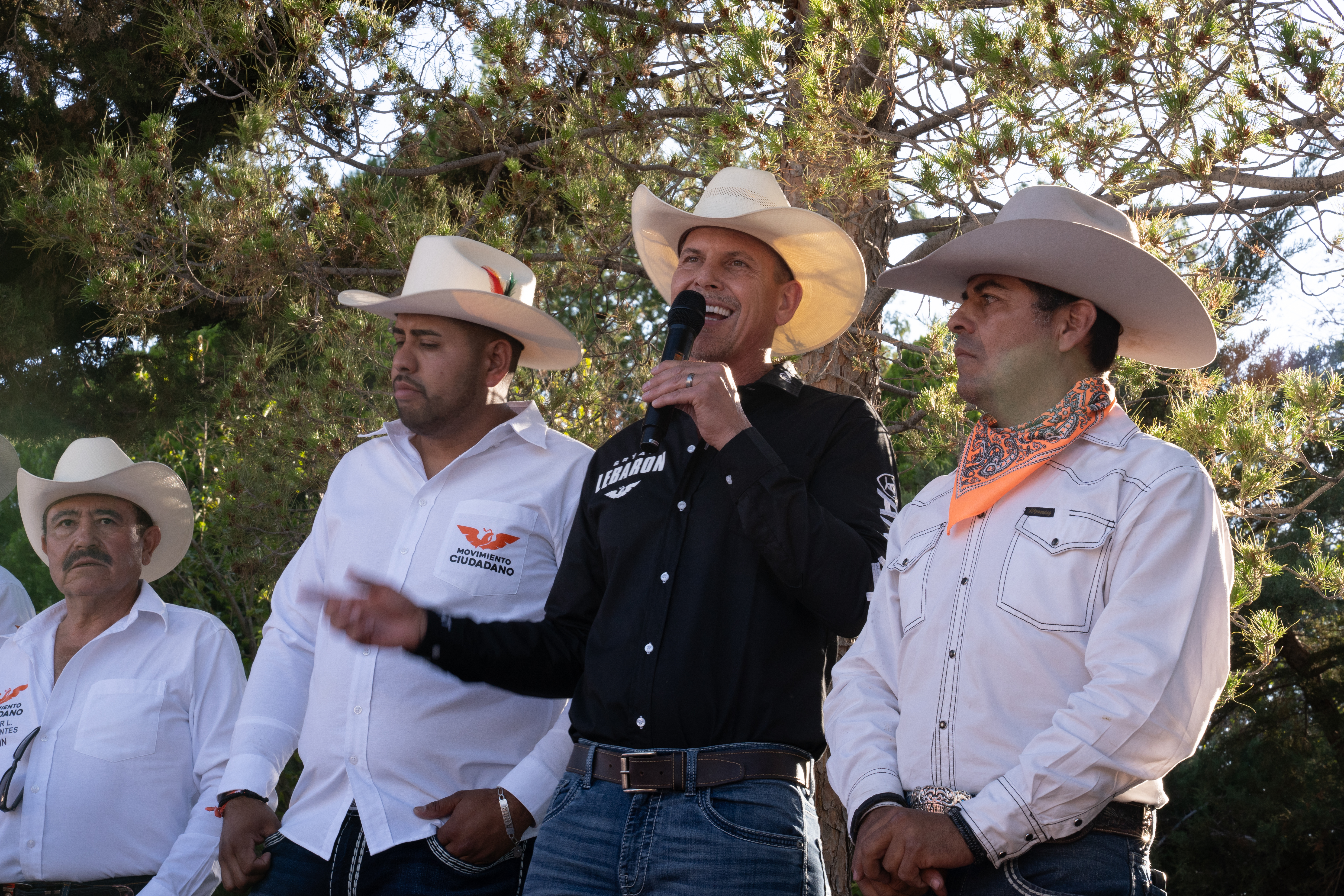 Brian LeBaron speaks into the microphone, surrounded by men in cowboy hats. 