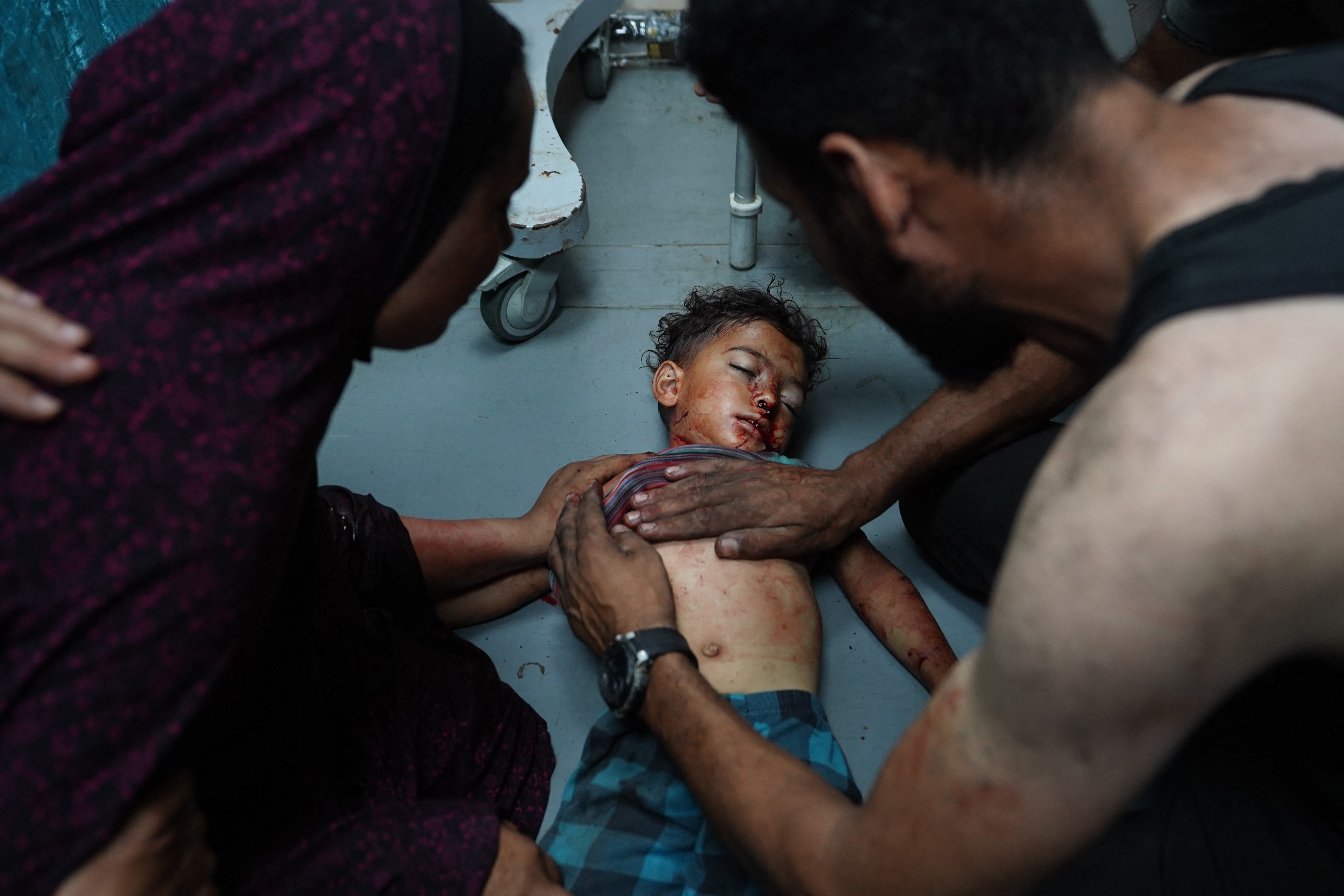 The mother of Palestinian toddler Khaled Abu Samaha holds his shoulder as a man tries to save his life at the Al-Aqsa Martyrs Hospital in the central Gaza Strip after he was badly injured in Israeli bombardment on a house in Nuseirat city on May 27