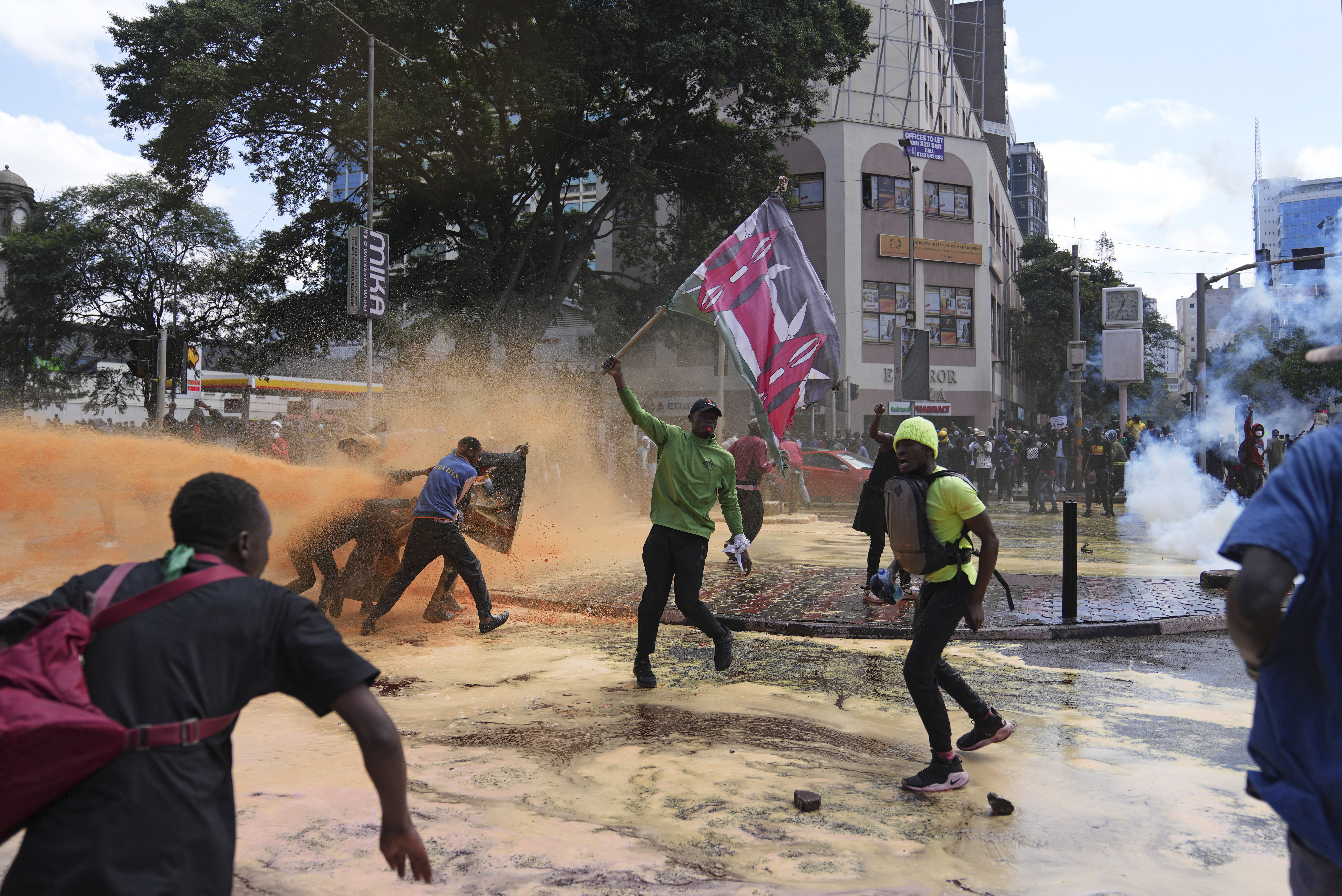 Protesters scatter as Kenya police spray a water canon at them during a protest over proposed tax hikes in a finance bill in downtown Nairobi, Kenya