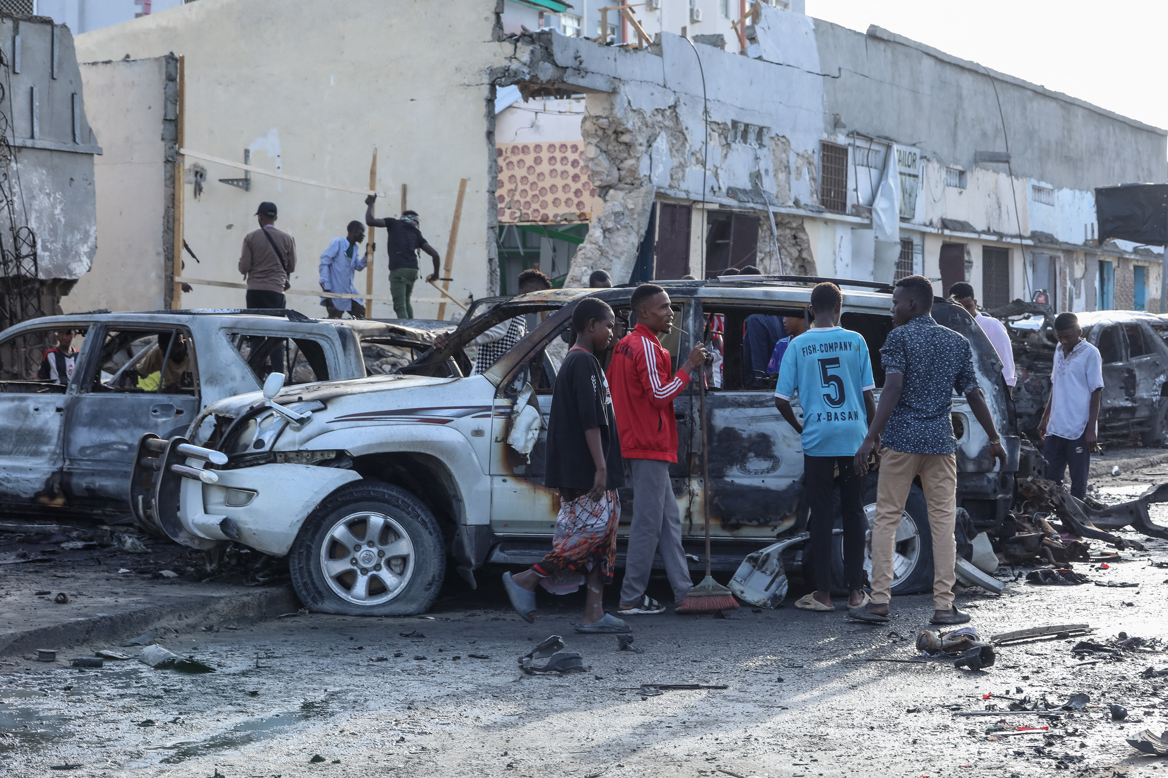 A group of people look at the debris and destruction at a cafe in Mogadishu on July 15, 2024 following a car bomb blast where five people were killed where football fans were watching the Euro 2024 final late on July 14, 2024. (Photo by Hassan Ali ELMI / AFP)