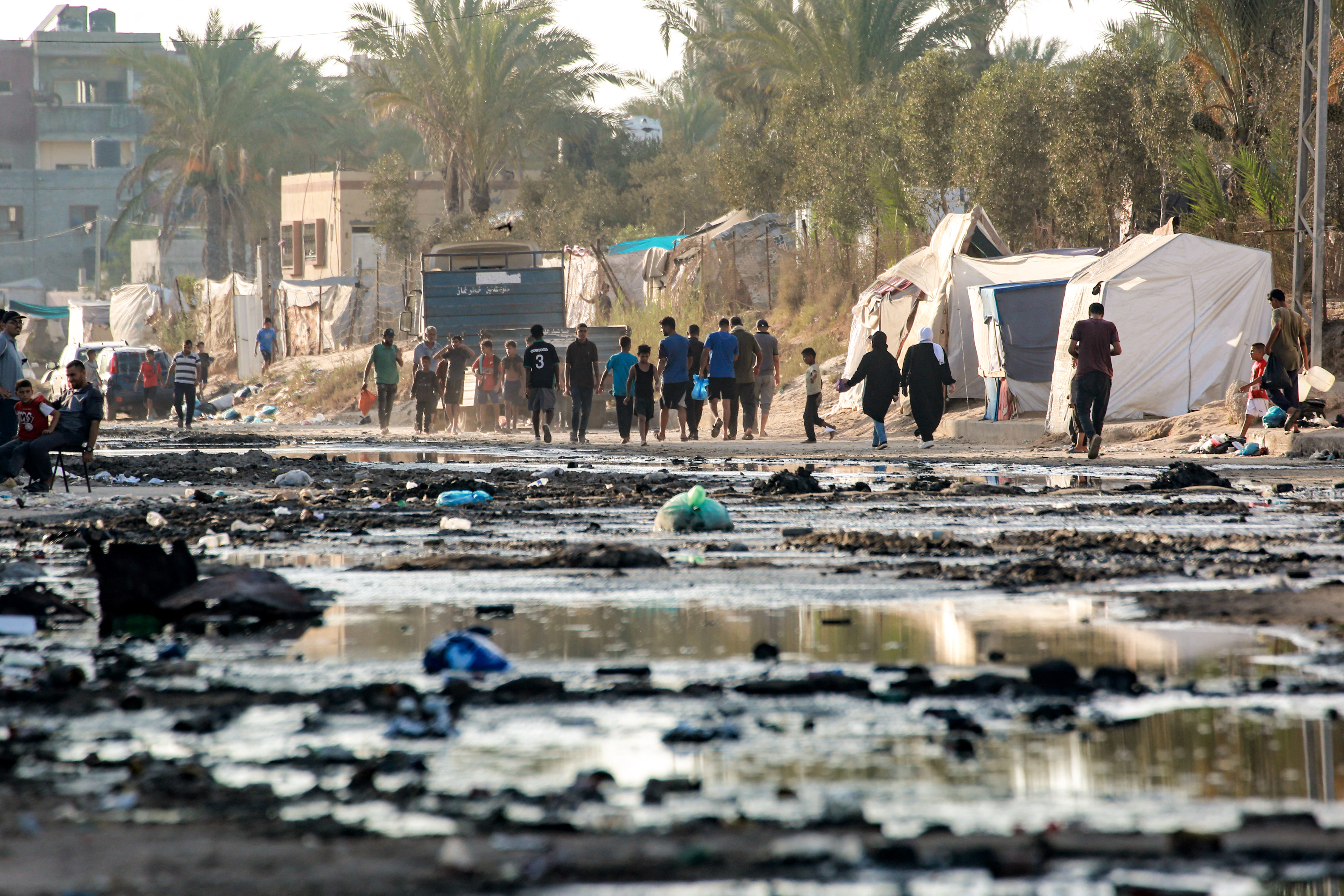 Palestinians walks near tents used as shelter along a street covered with stagnant wastewater in Deir el-Balah in the central Gaza Strip on July 19, 2024. [Bashar Taleb/AFP]