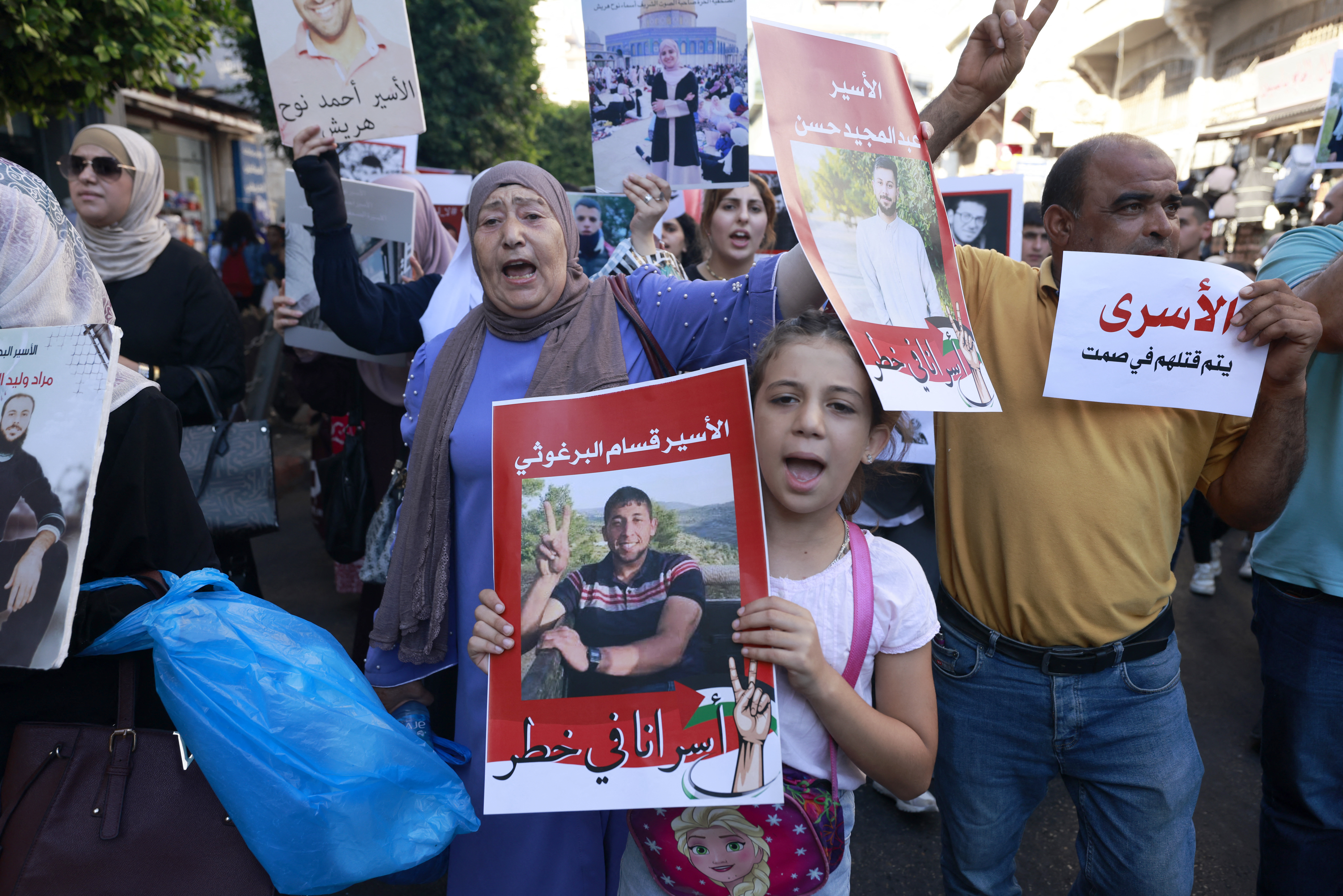 people hold photographs at a protest in a street