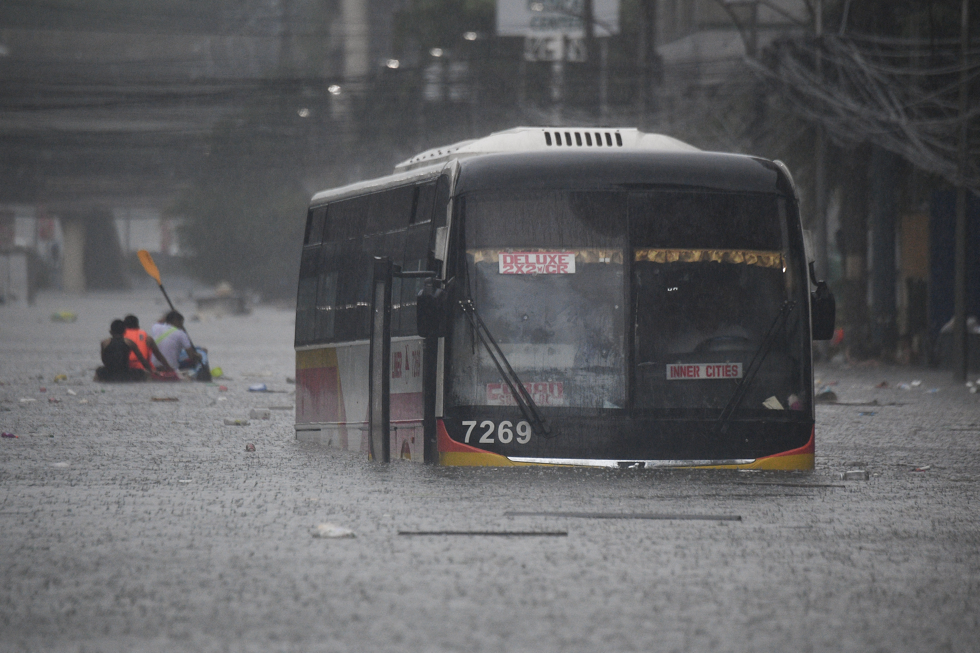 People paddle a boat past a half-submerged passenger bus along a flooded street in Manila on July 24, 2024 amid heavy rains brought by Typhoon Gaemi. Relentless rain drenched the northern Philippines on July 24, triggering flooding in Manila and landslides in mountainous regions as Typhoon Gaemi intensified the seasonal monsoon. (Photo by Ted ALJIBE / AFP)