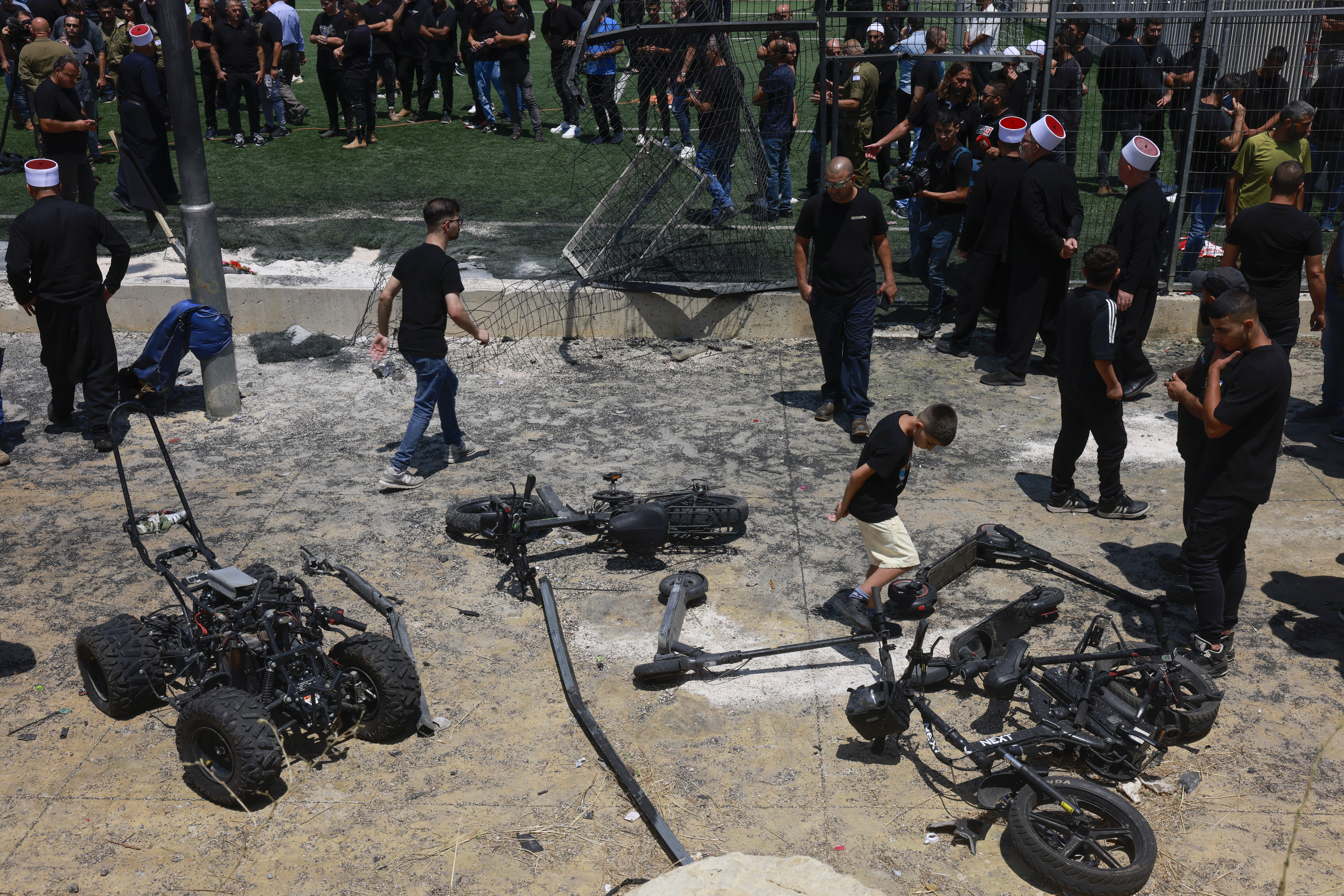 Members of the Druze community look at the damaged fence and scattered objects at a football pitch, a day after 12 people were killed there in a rocket strike from Lebanon, in the Druze town of Majdal Shams in the Israel-annexed Golan Heights, on July 28, 2024.