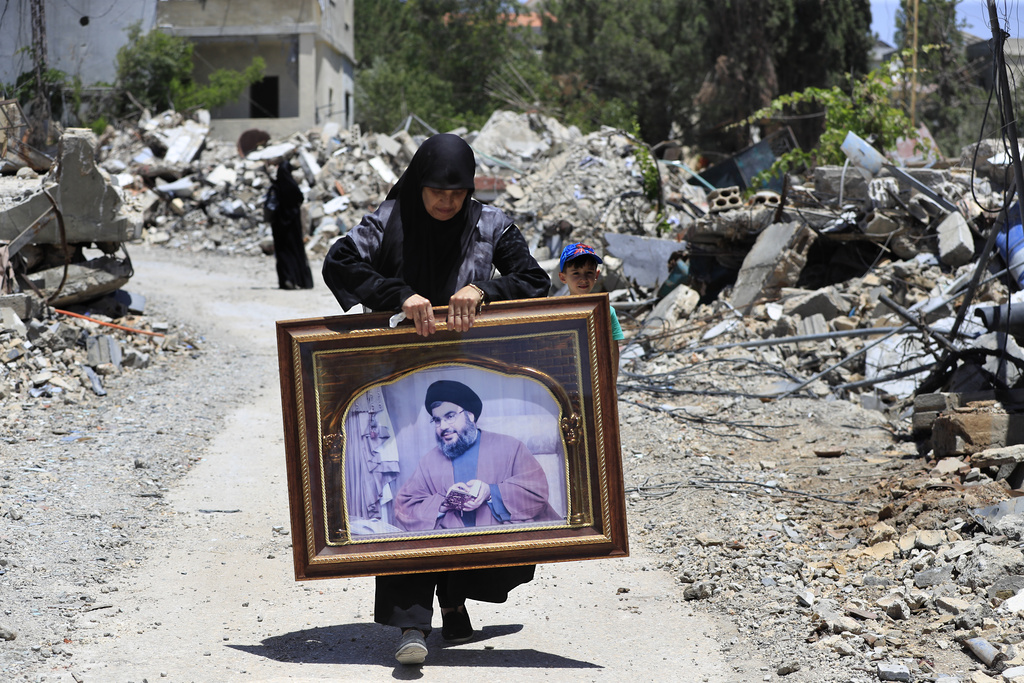 a woman carries a portrait of a man through a destroyed street