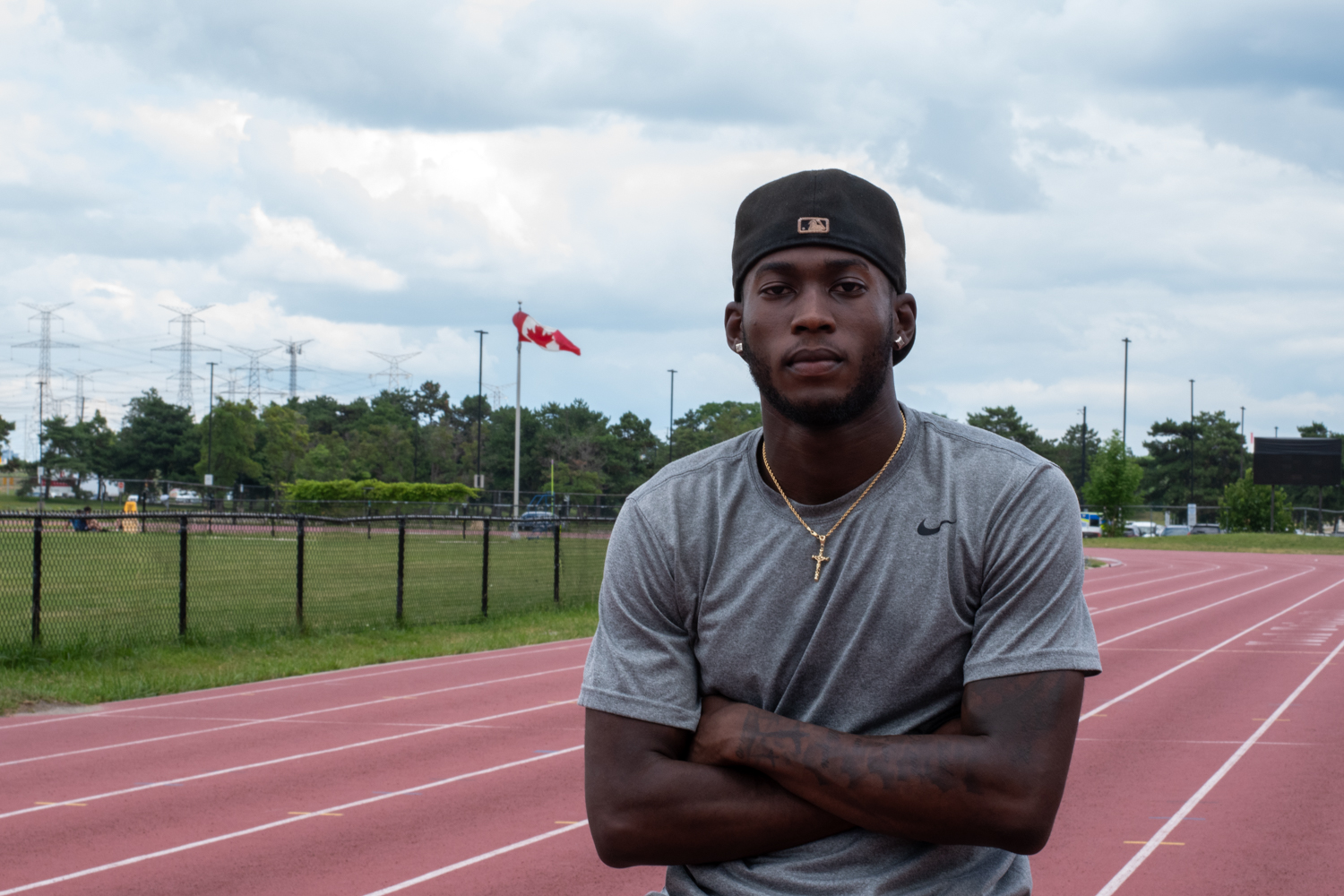 Tamarri stands on an outdoor track cross-armed. Behind him is a flag pole bearing the Canadian flag