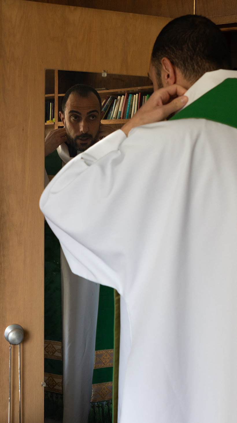 Pastor Khalilia adjusts the green sash on the white, flowing robes he wears for church service.
