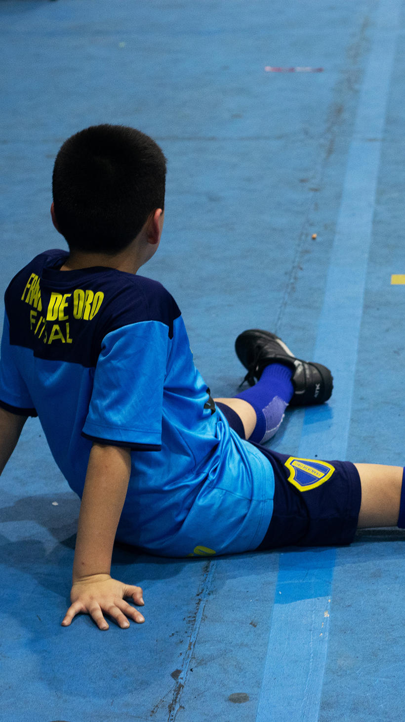 A boy from the Franja de Oro club sits on the floor of the indoor soccer field.