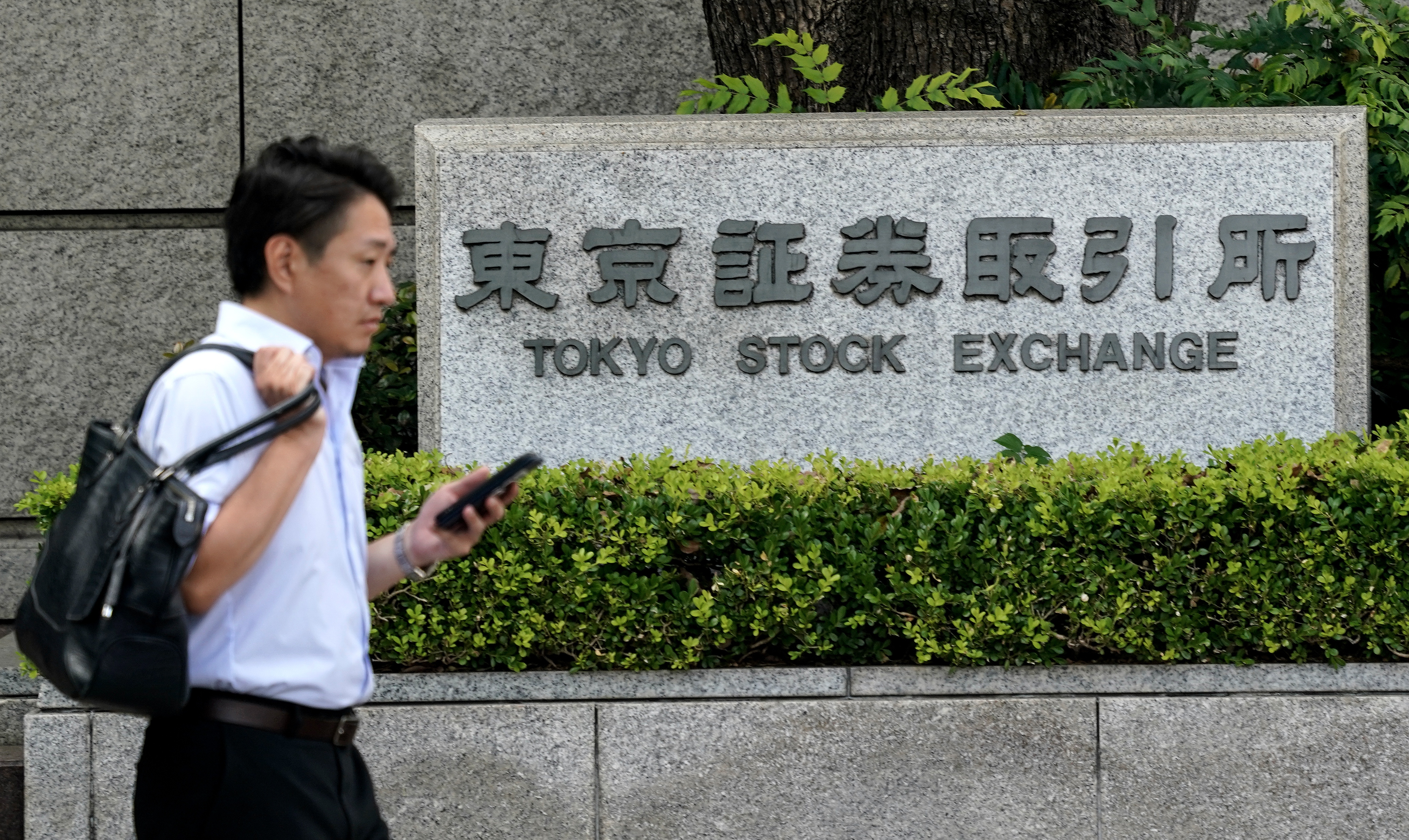 A man walks past the sign for the Tokyo Stock Exchange